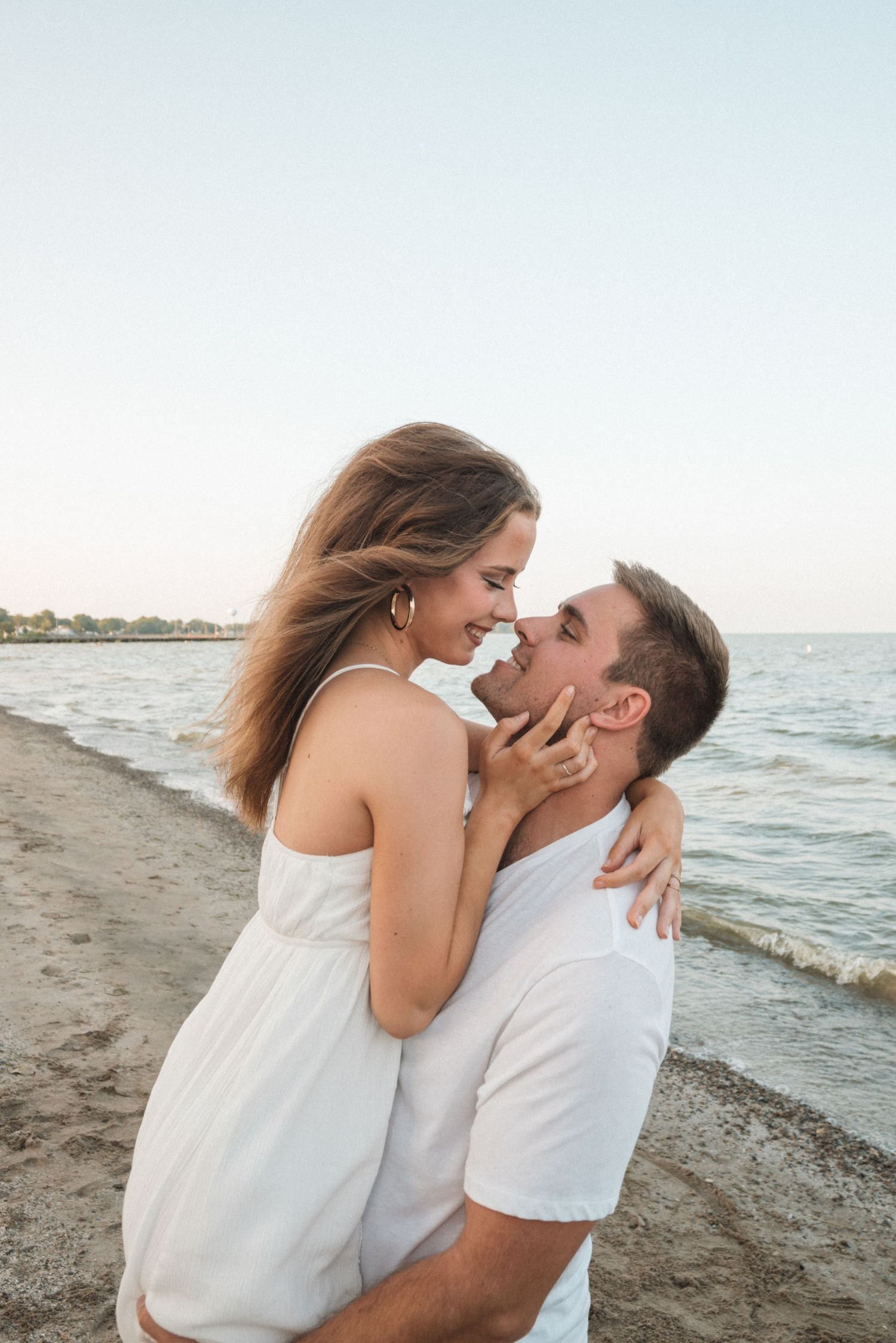 Couple sharing an intimate moment on a beach at sunset with ocean waves in background.