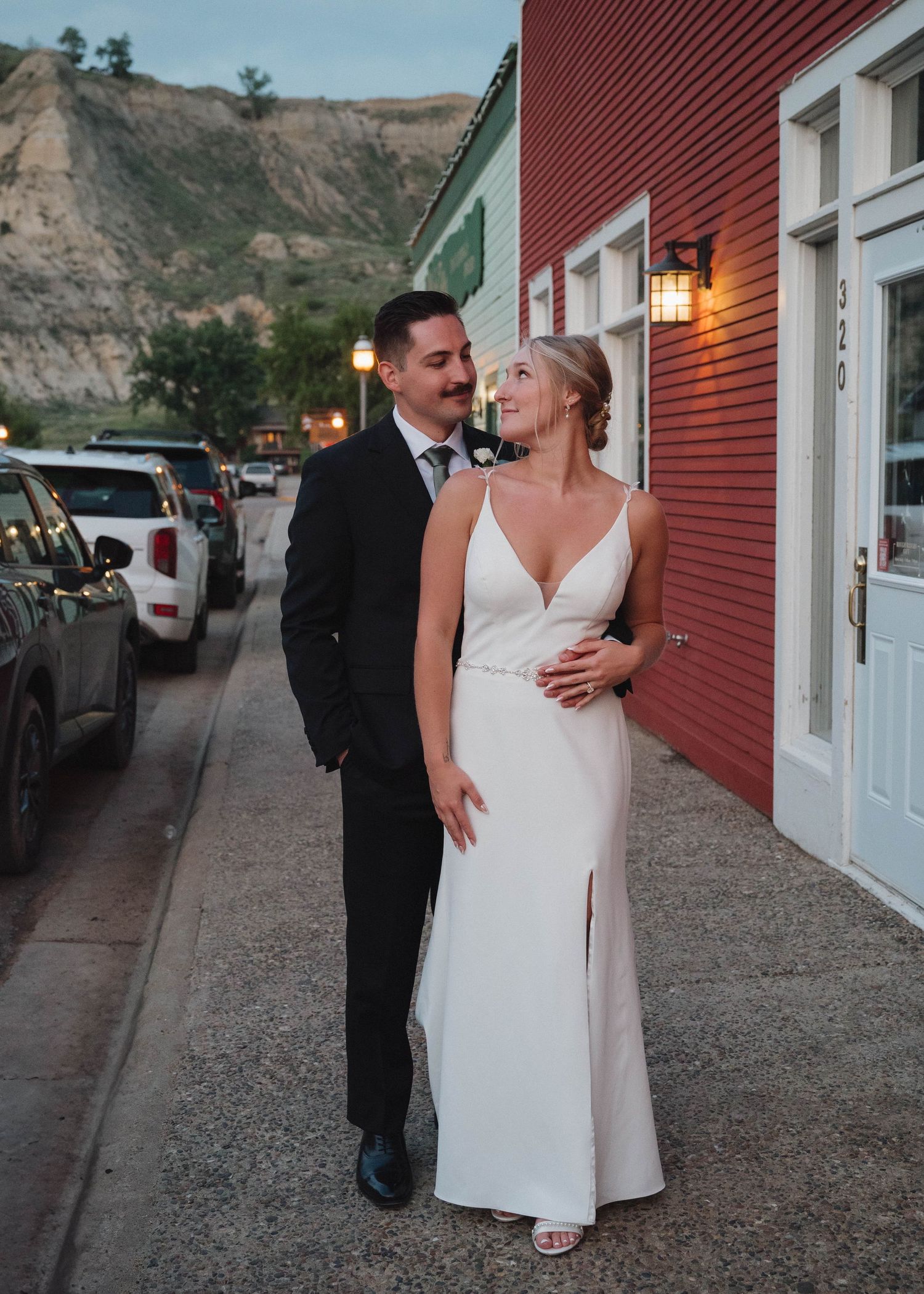 A couple shares romantic moments outside a red barn-style building at dusk with glowing lanterns illuminating the scene.