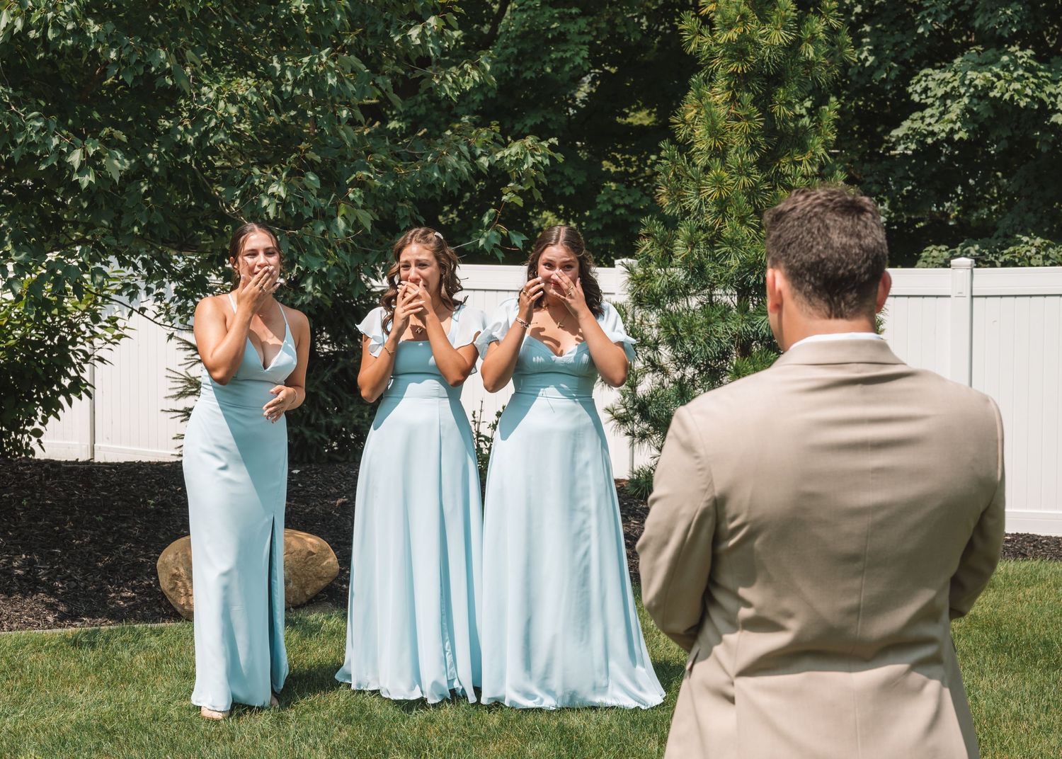 Wedding party in light blue bridesmaid dresses posing outdoors on a sunny day.