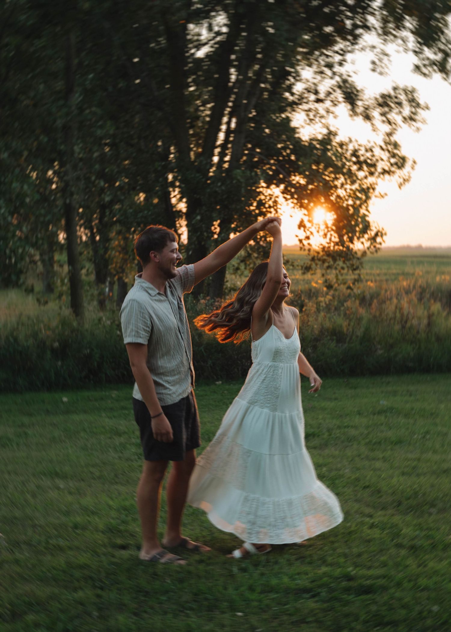 Dancing couple twirls and embraces in a dreamy outdoor setting with trees and sunset light.
