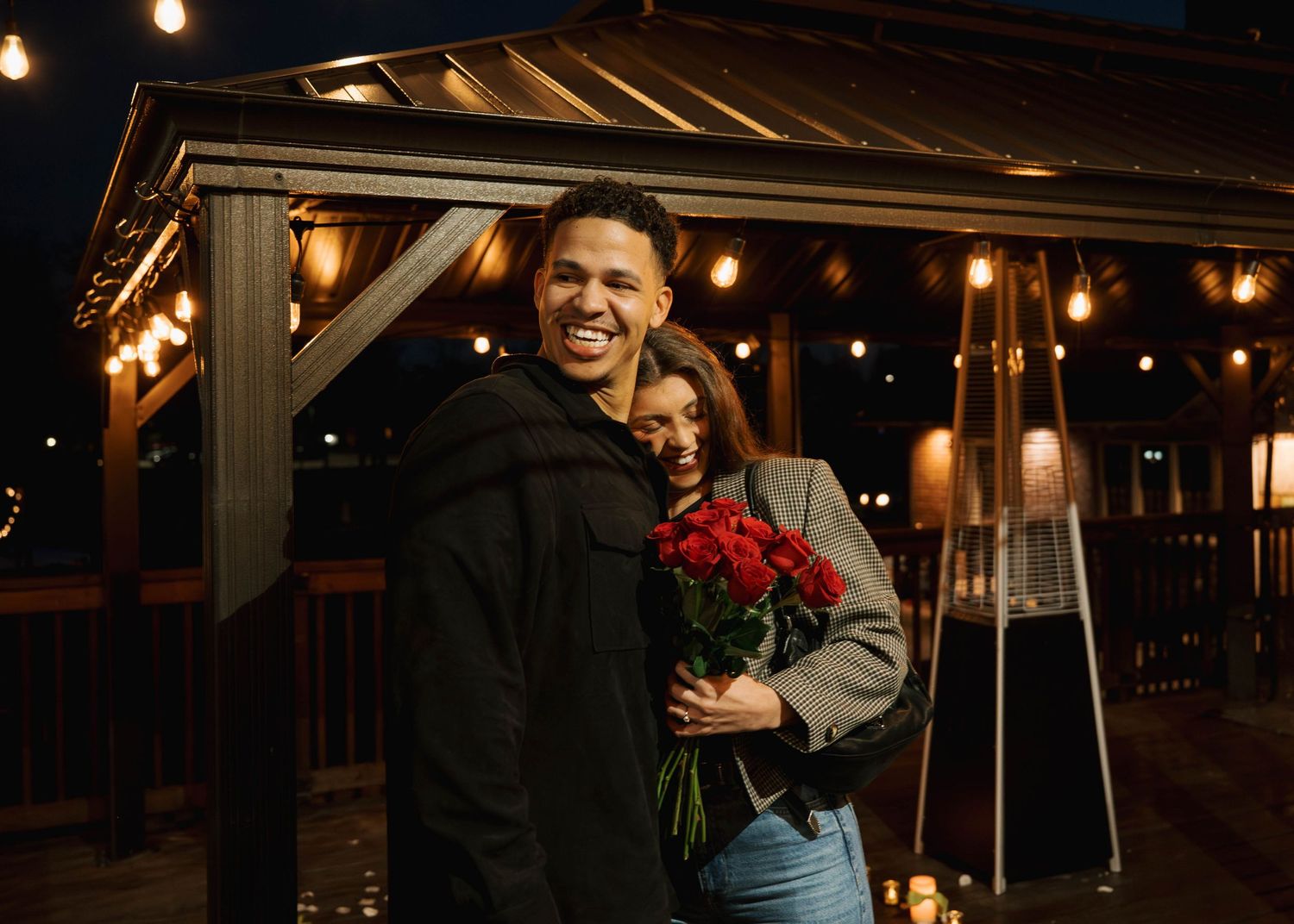 Couple sharing intimate moment under string lights with roses at night.