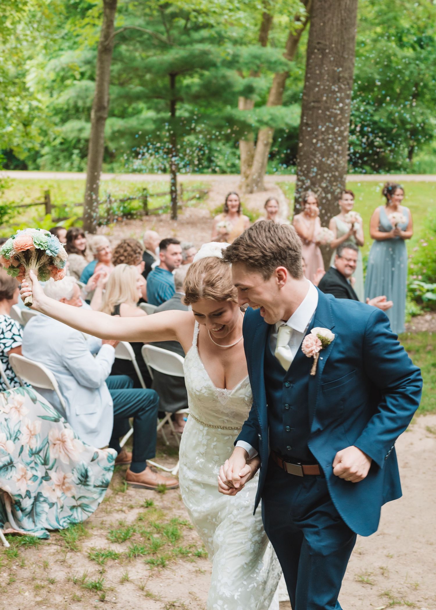 A joyful couple celebrates with guests during their outdoor forest wedding ceremony.