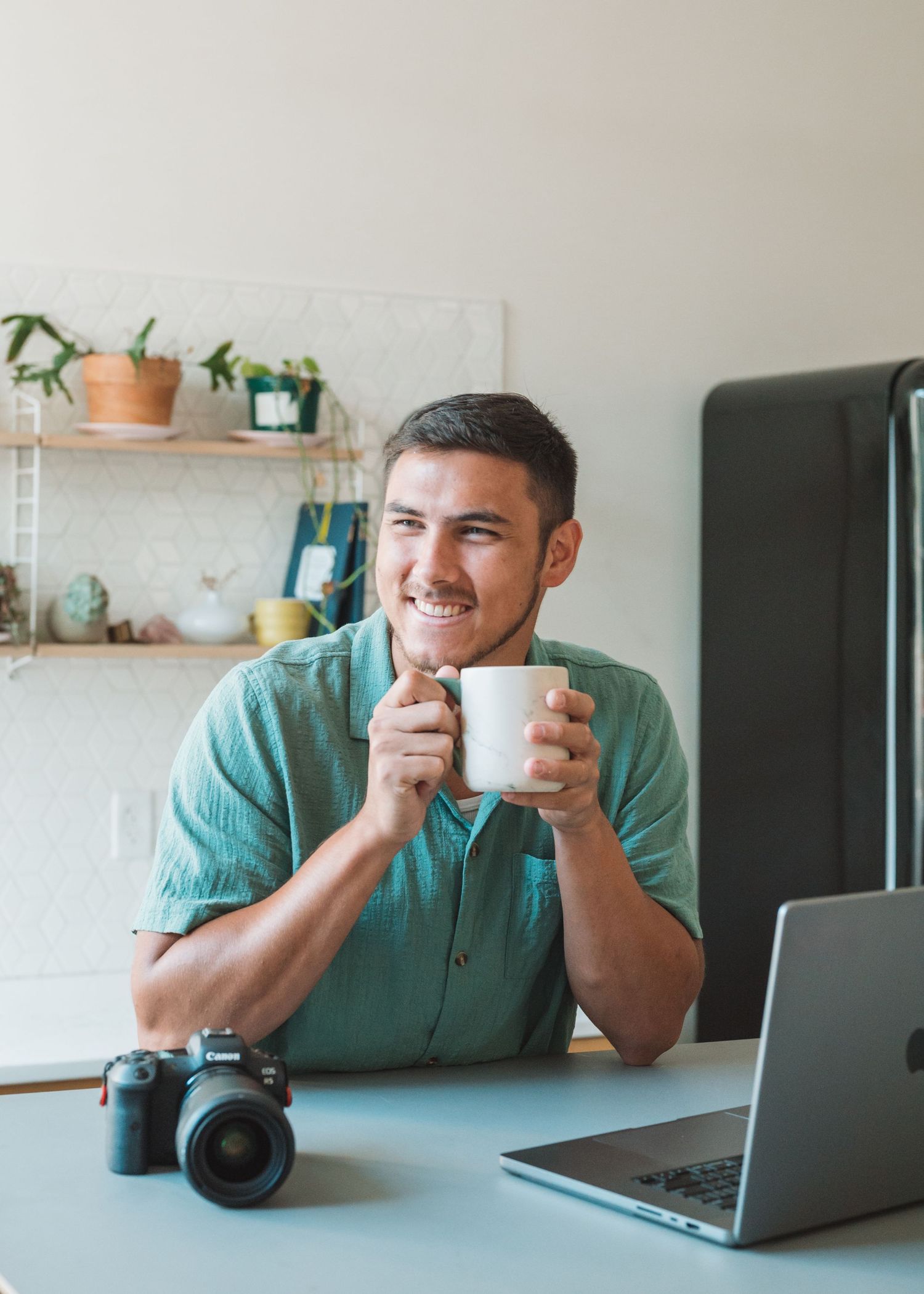 Person enjoying coffee at desk with laptop and camera in modern home office.