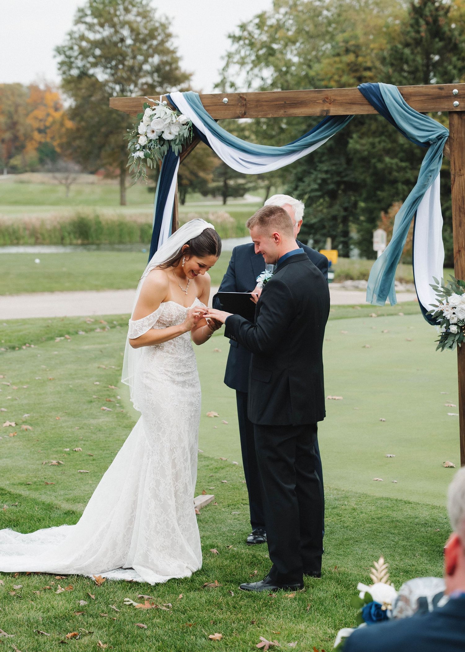 A couple shares a dance together on a golf course with blue drapery and autumn trees in the background.