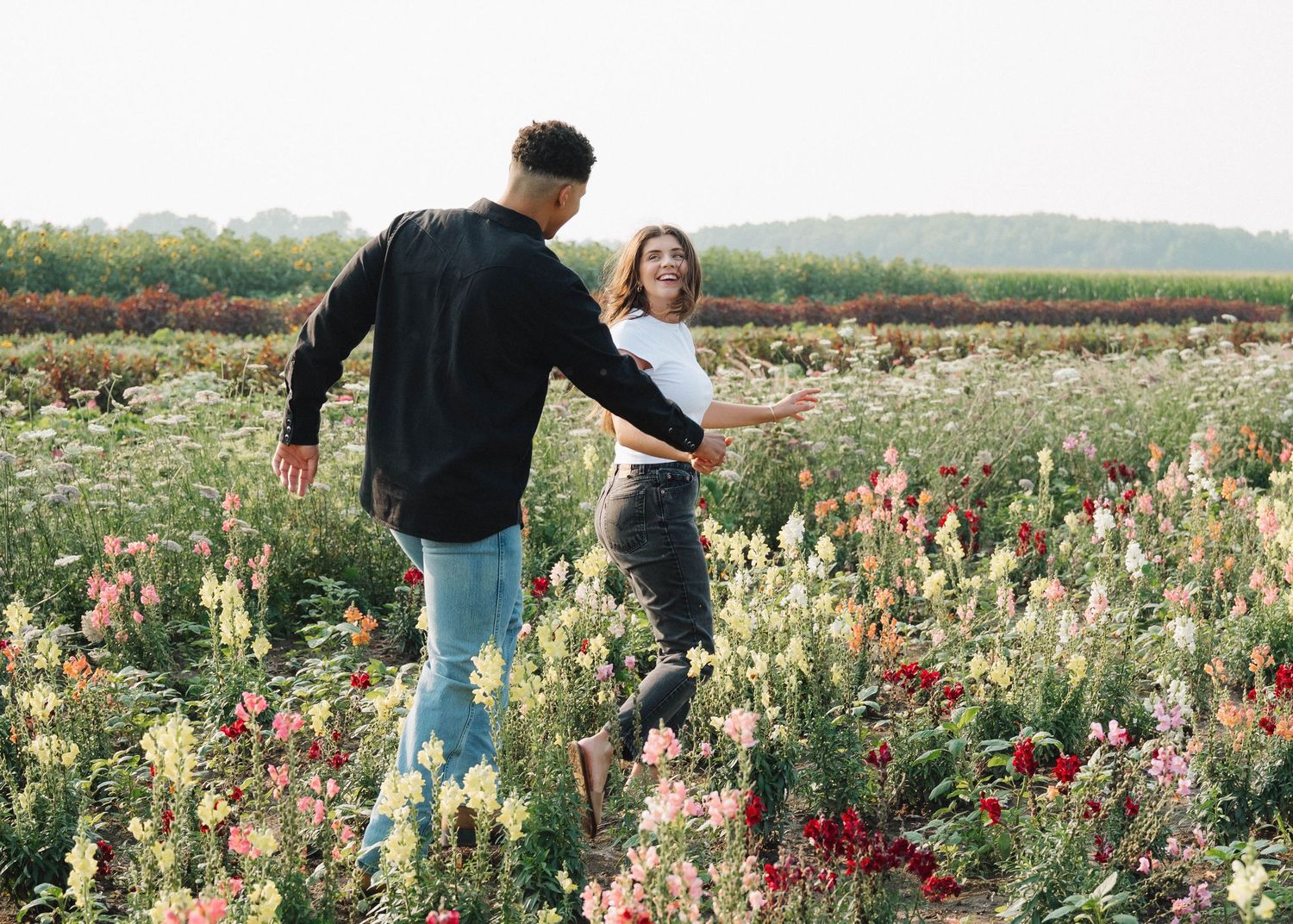 People walking through a colorful wildflower field filled with blooming red and pink flowers on a sunny day.