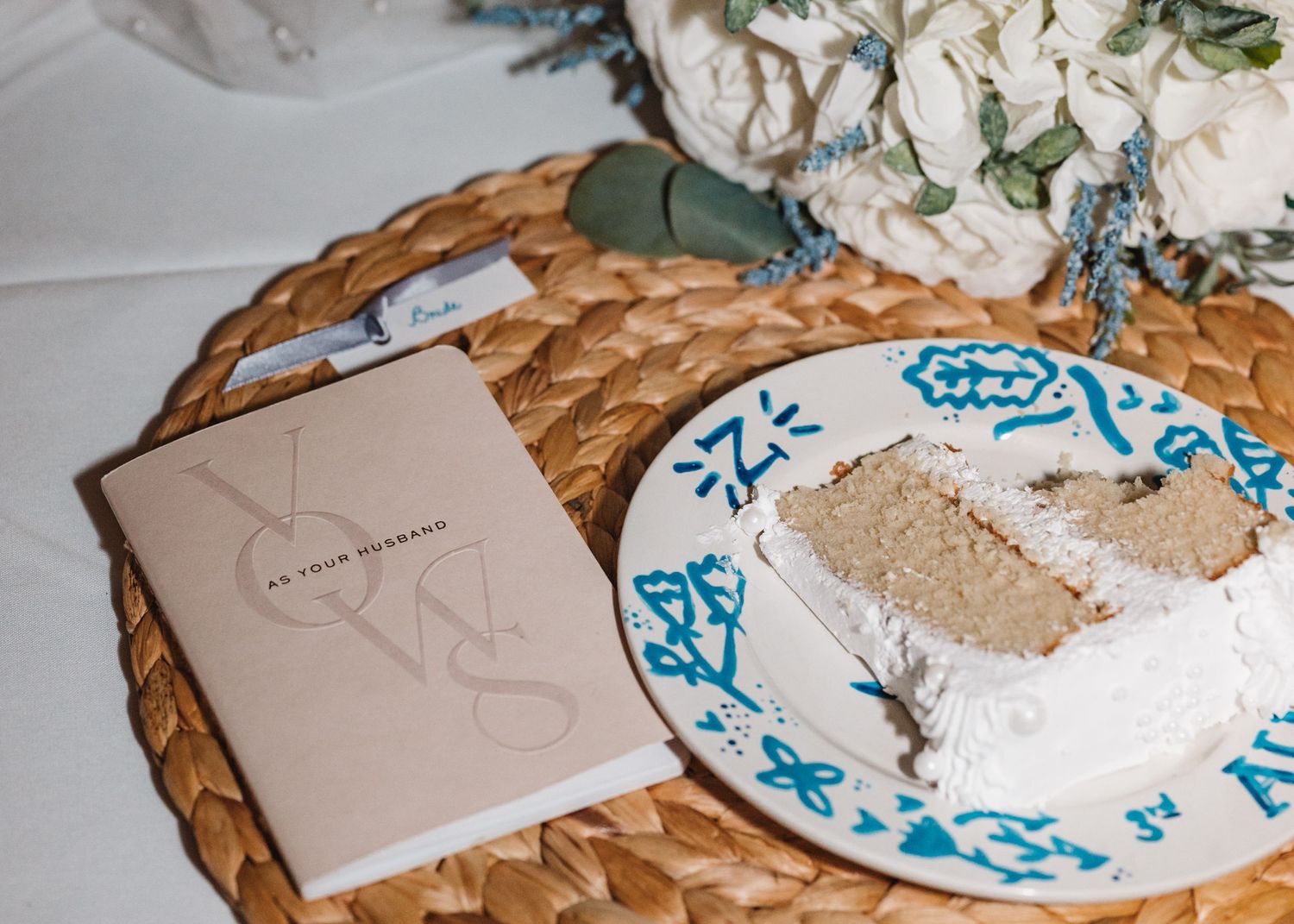 Wedding details featuring vow book and slice of cake on decorative plate with blue accents.