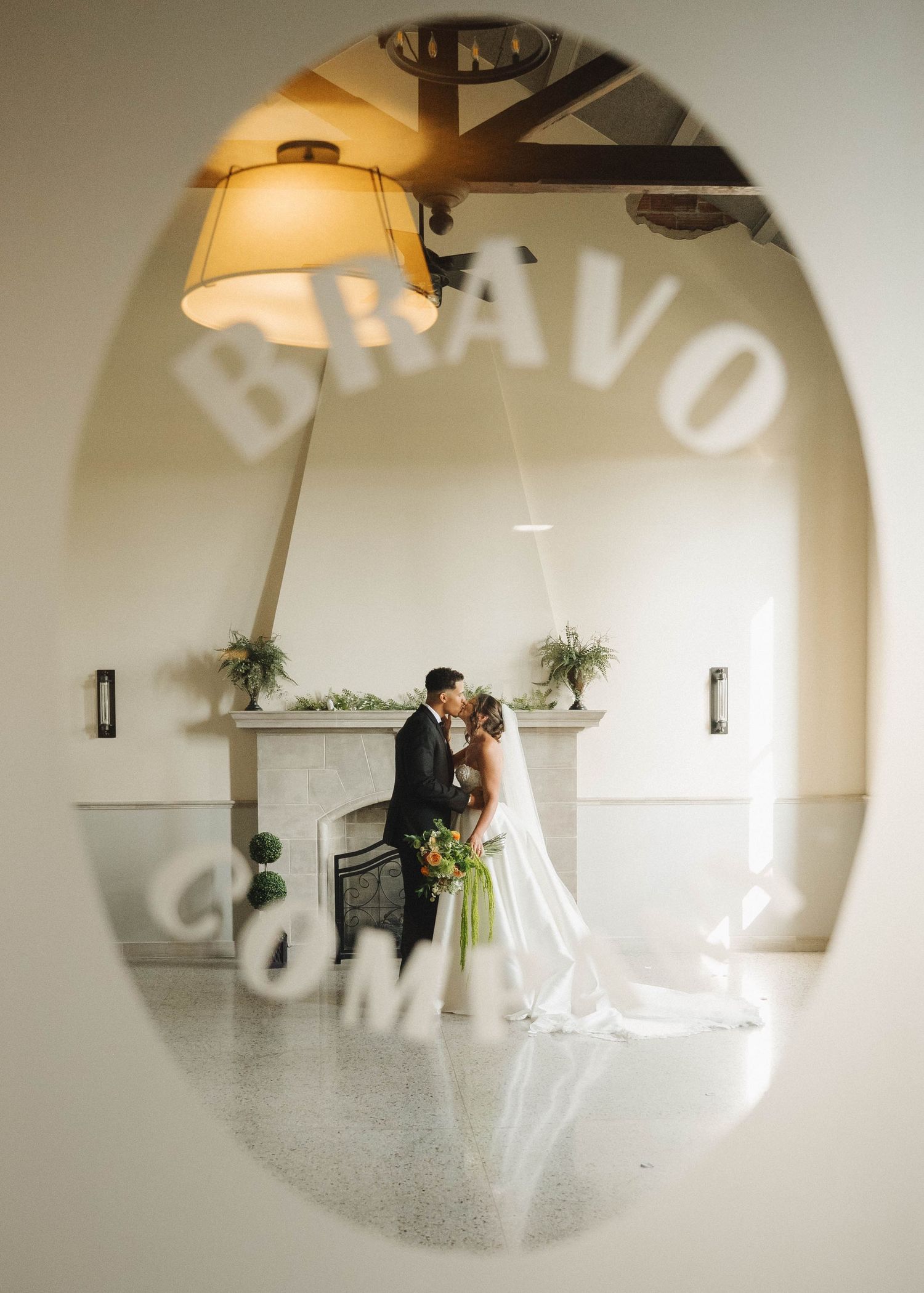 A romantic wedding scene captured through an oval frame with the word 'BRAVO' casting a shadow on white walls.
