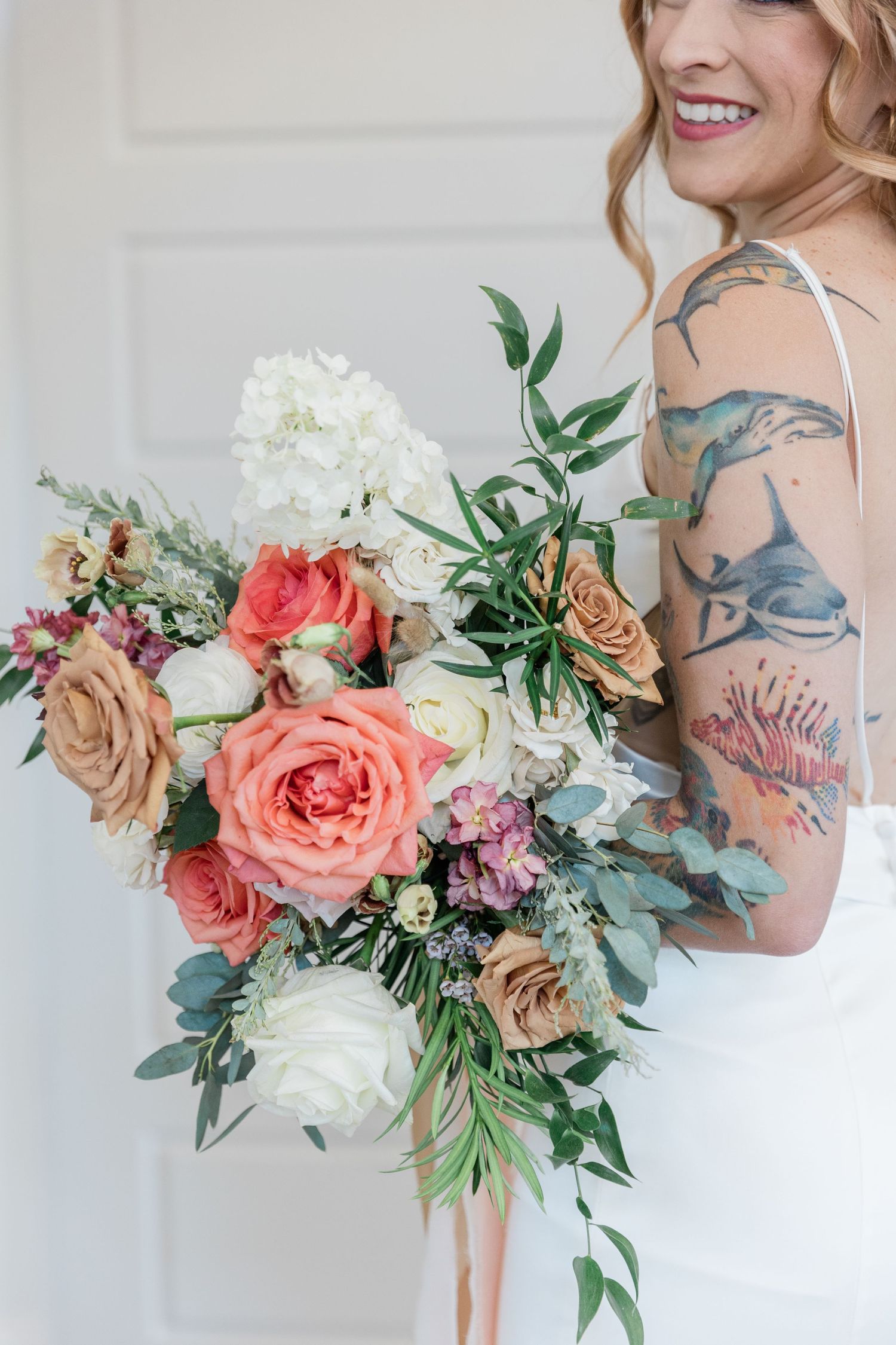 Close-up of bridal bouquet featuring colorful roses resting in her arms with her lace dress as a backdrop.
