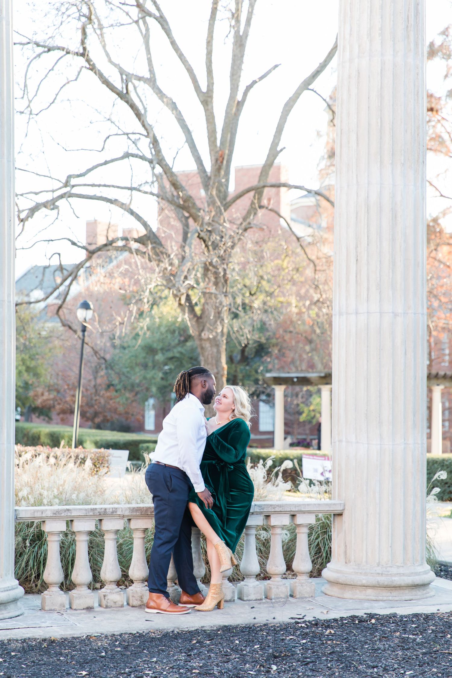 Full body shot of the bride and groom sitting down at the Texas Women's University campus for their engagement session.