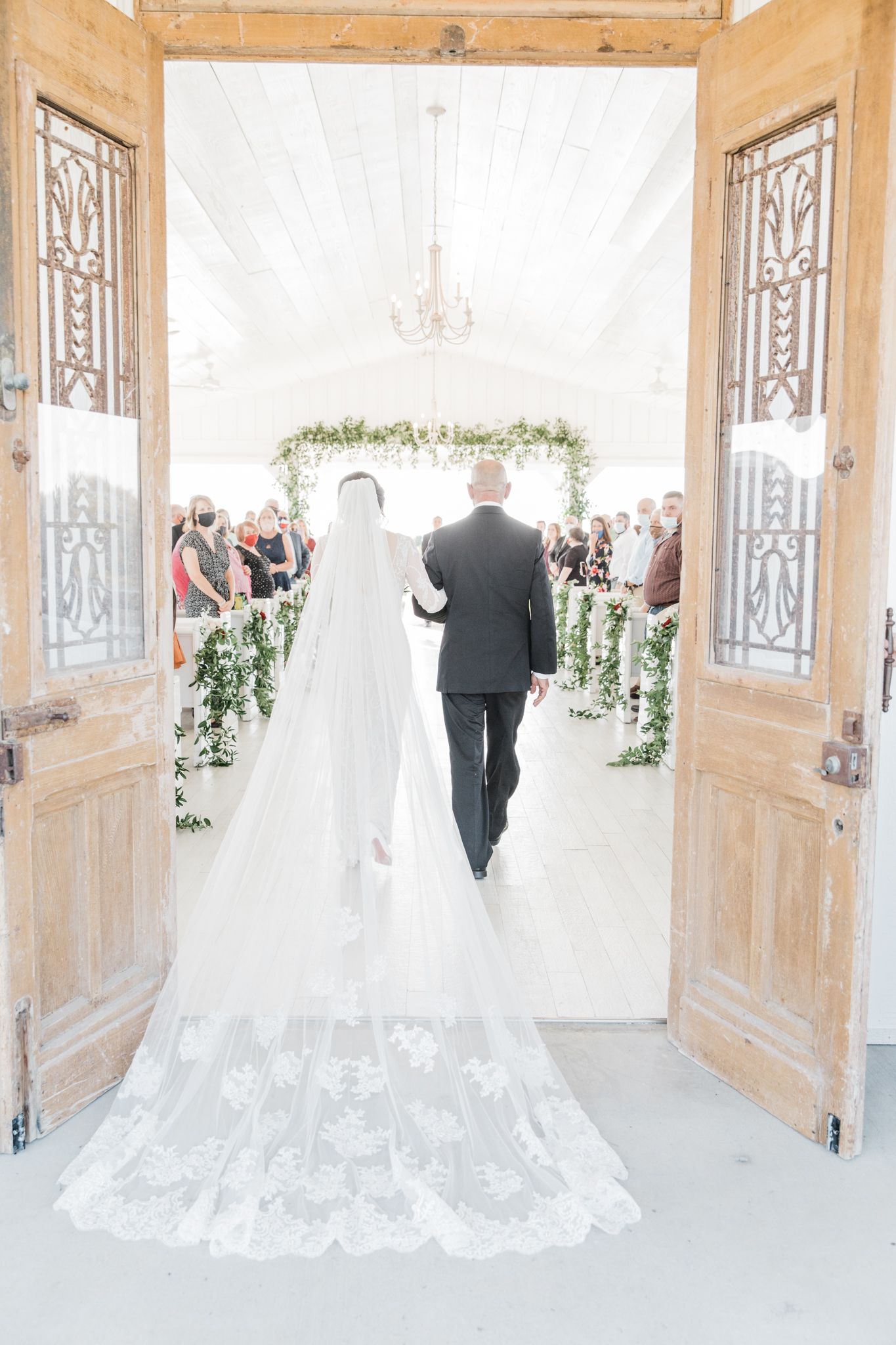 Bride and her father doing their walk down the aisle with a behind view of the bride's dress and long veil.