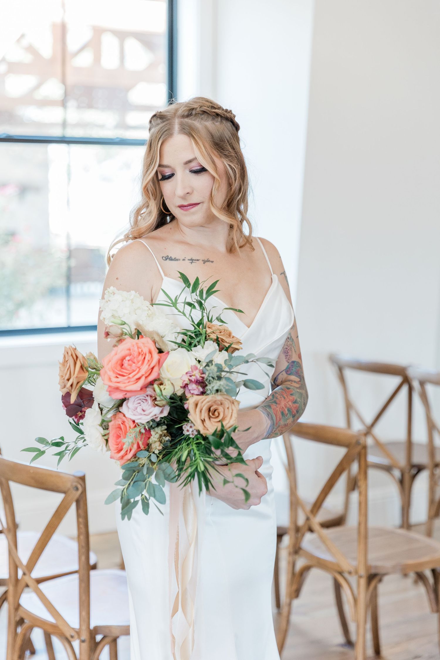 Close-up of bridal bouquet featuring colorful roses resting in her arms with her lace dress as a backdrop.