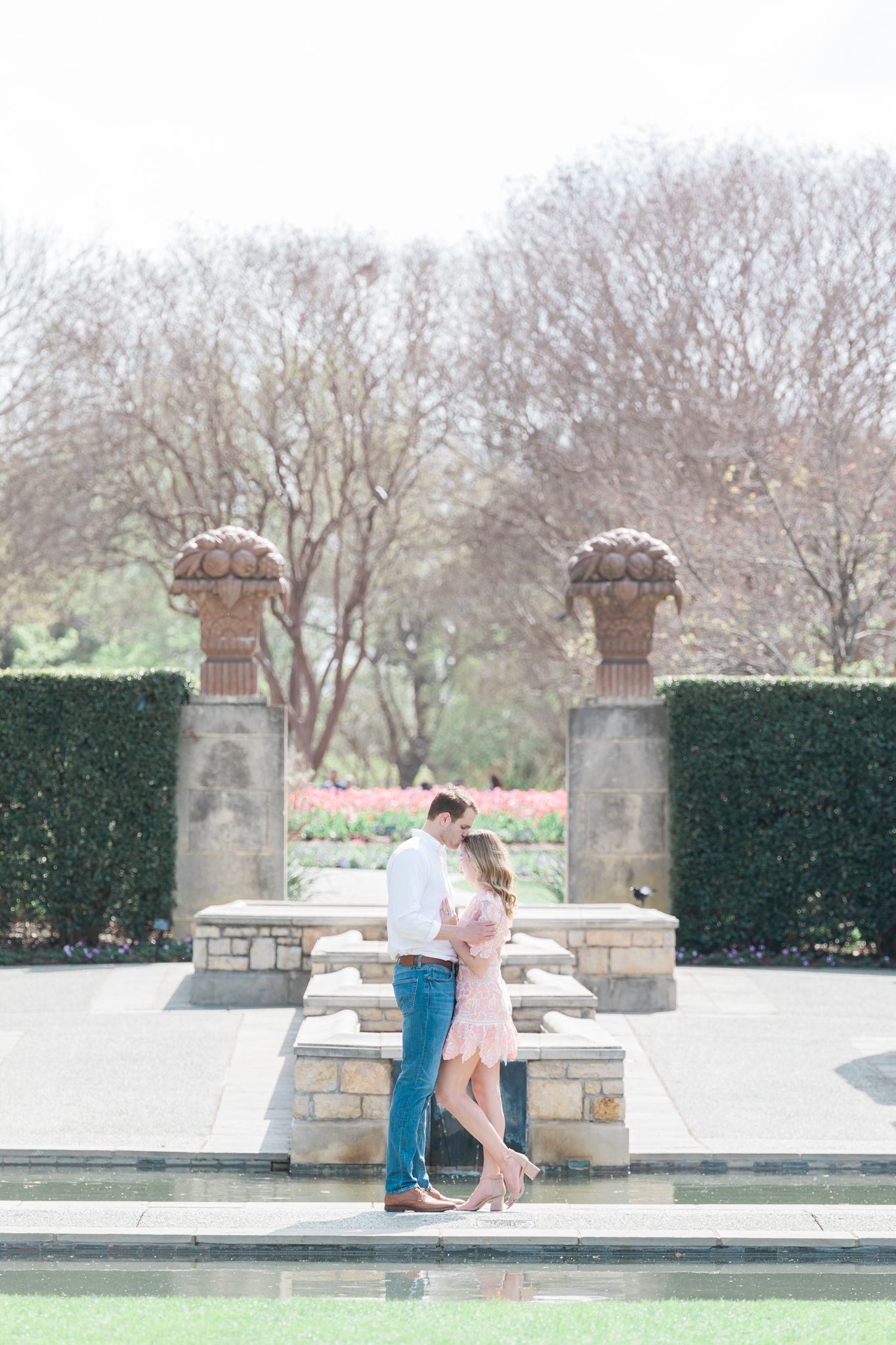 engaged couple sharing a joyful moment next to the reflecting pond at the Dallas Arboretum and Botanical Gardens.