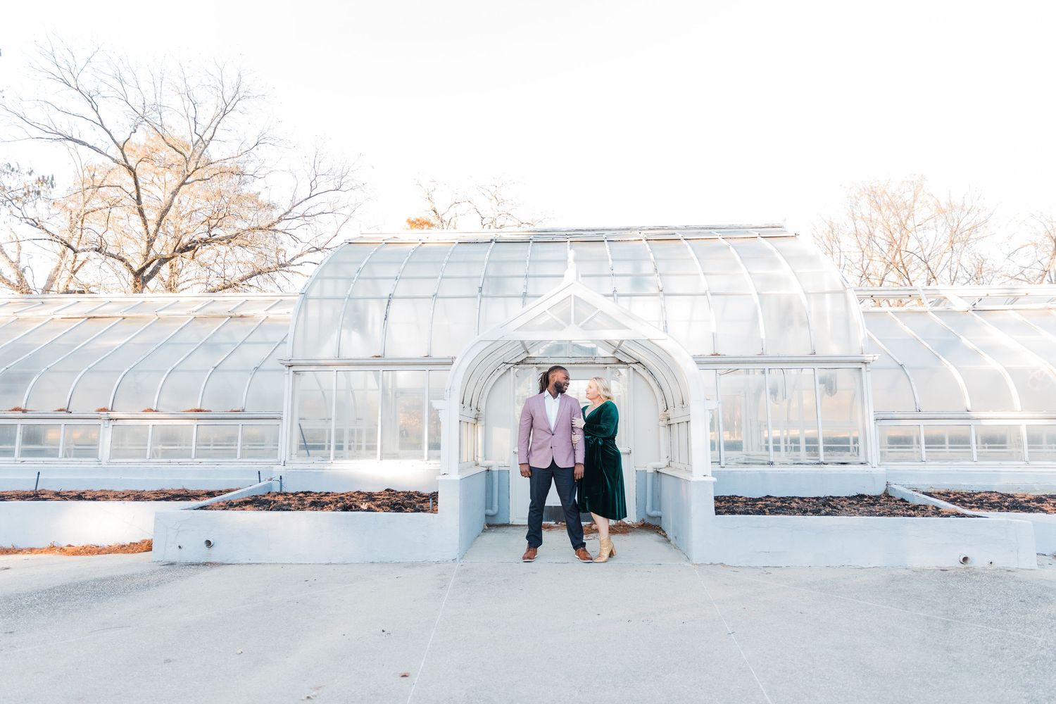 Wide full shot of the TWU greenhouse with a full body shot of the bride and groom looking at each other for their spring engagement session.
