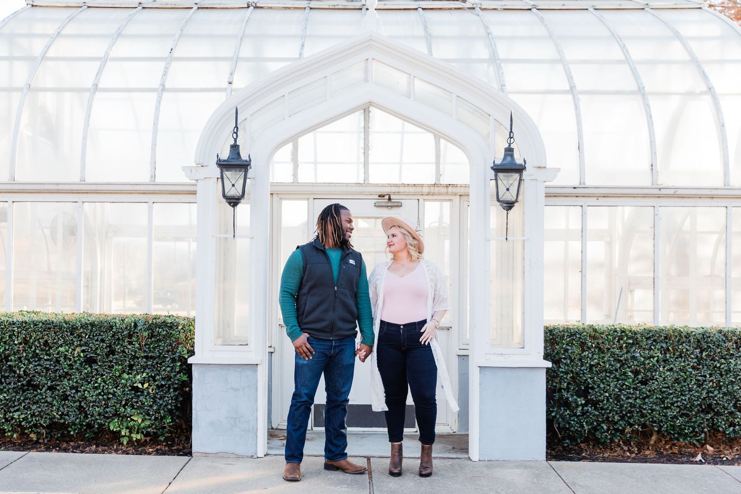 Full body shot of the bride and groom in front of the Texas Women's University greenhouse for their engagement session.