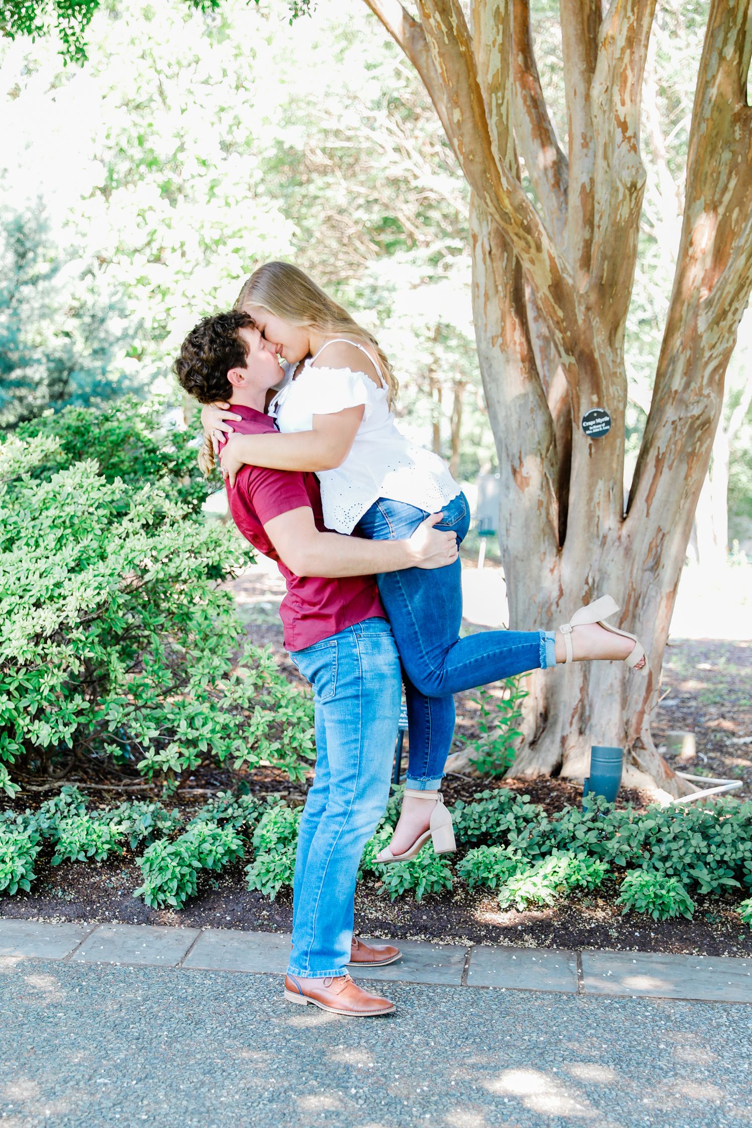 Groom picking up bride for a lifting kissing picture at the Dallas Botanical Gardens for a fall engagement Session.