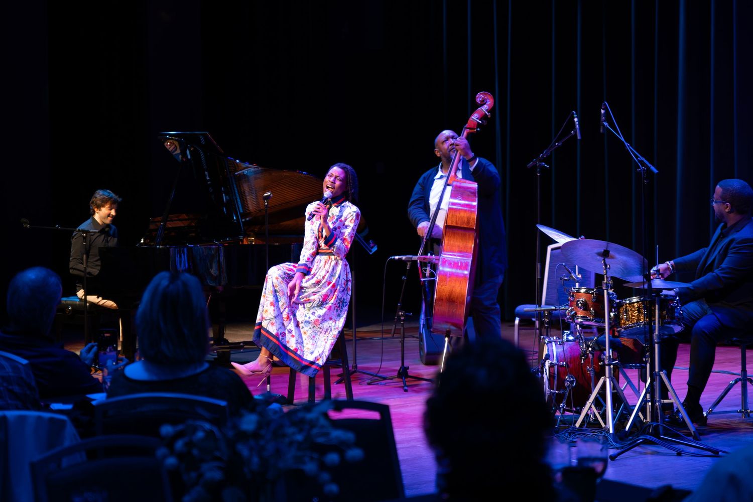 Musicians perform on a dimly lit stage with blue lighting and musical instruments.