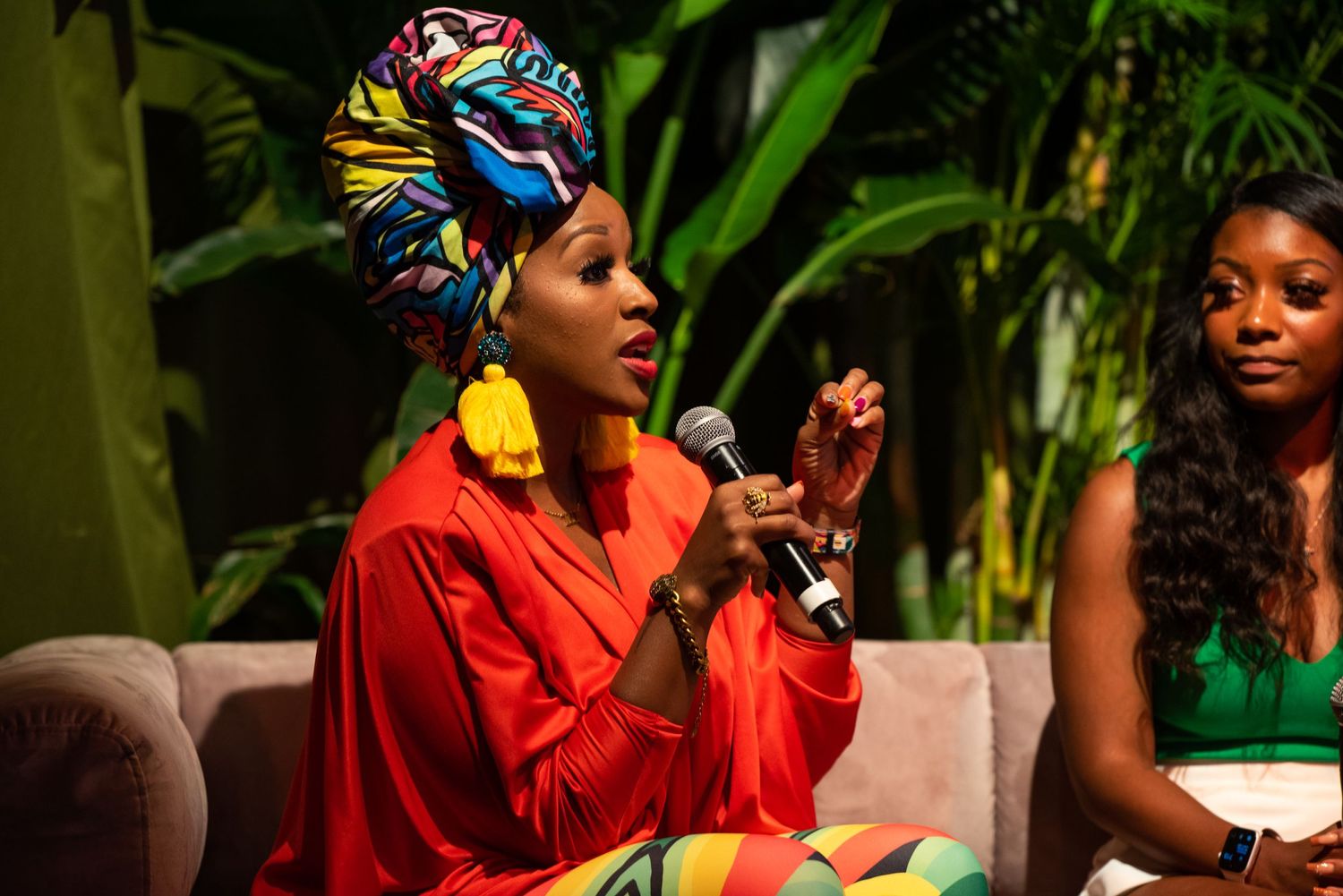 Musicians perform on stage with tropical plants in the background.