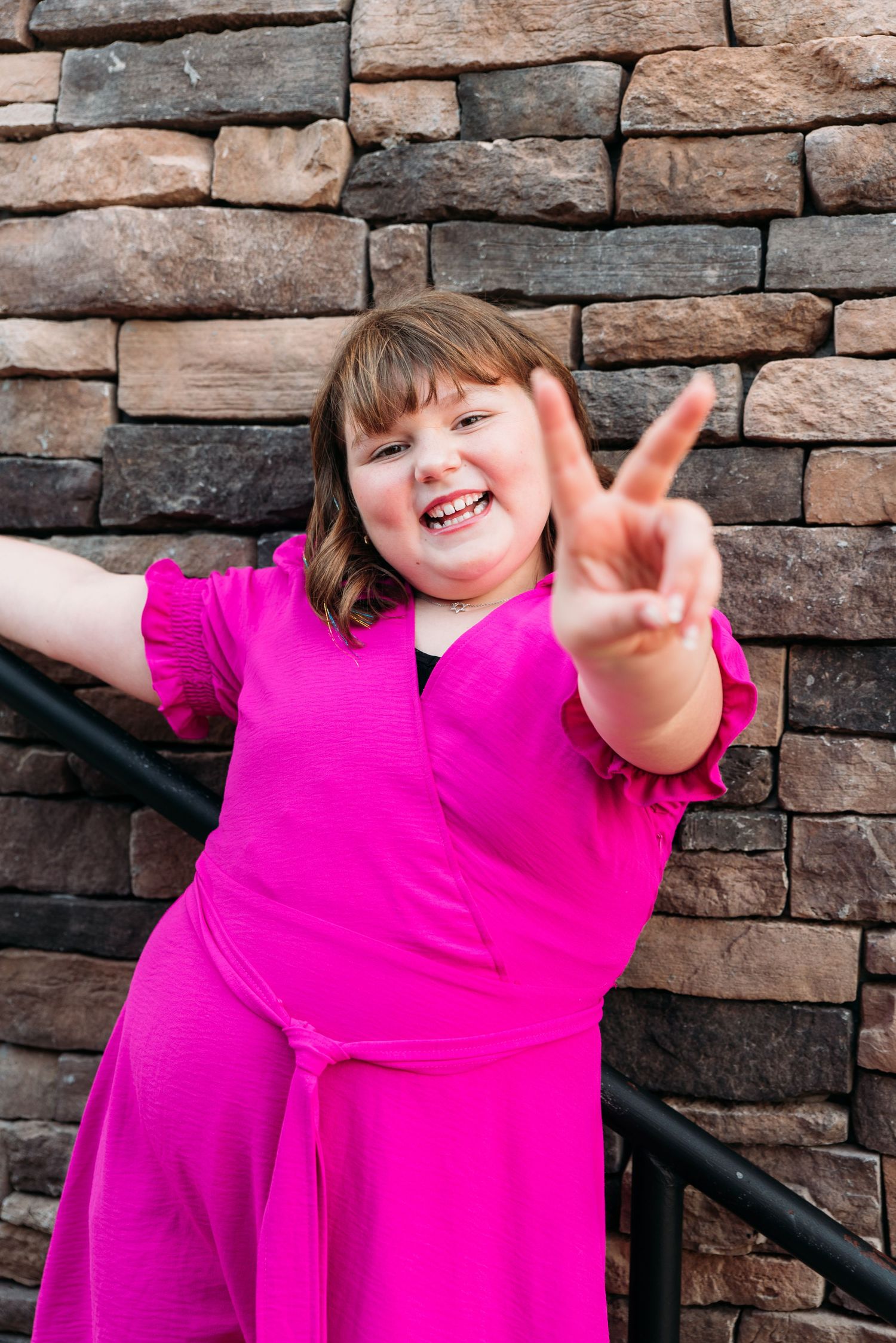 Person in bright pink shirt posing expressively against stone wall.