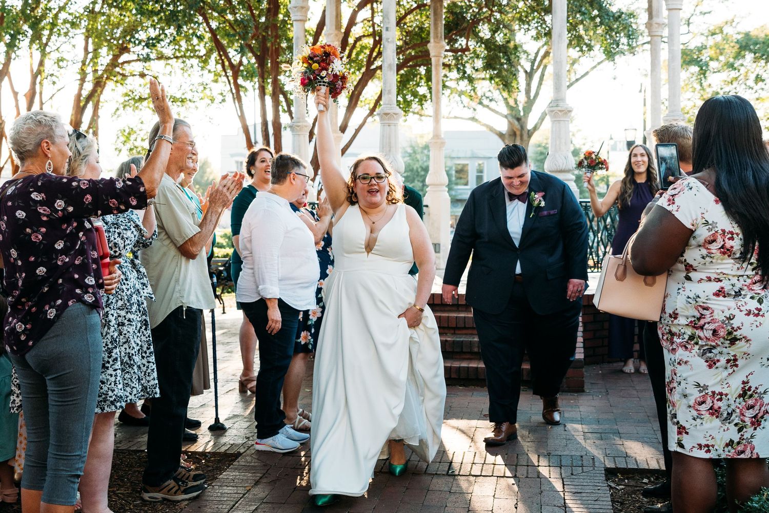 Wedding guests dance and celebrate at an outdoor reception with string lights overhead.