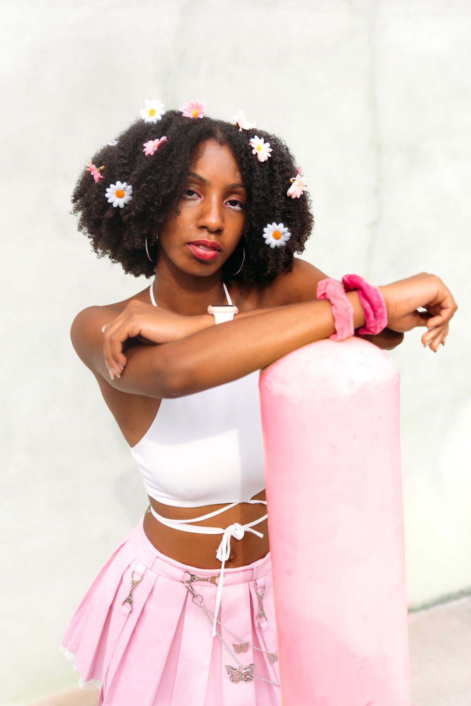 Artistic portrait with daisies adorning natural hair against white background.