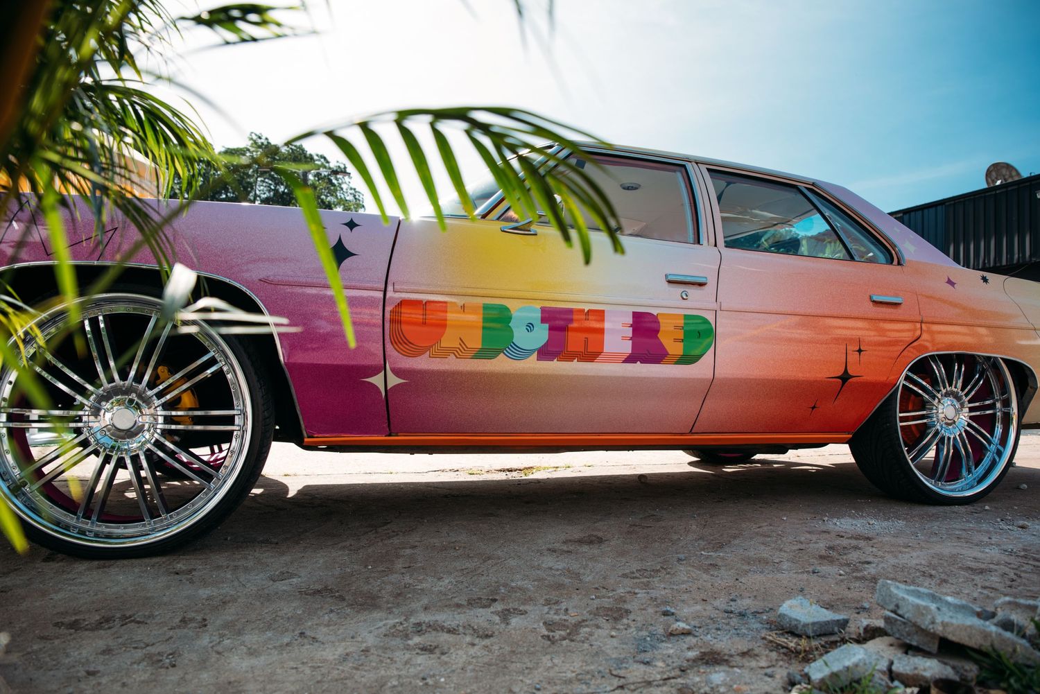 Row of colorful lowrider cars with custom paint jobs displayed outdoors.