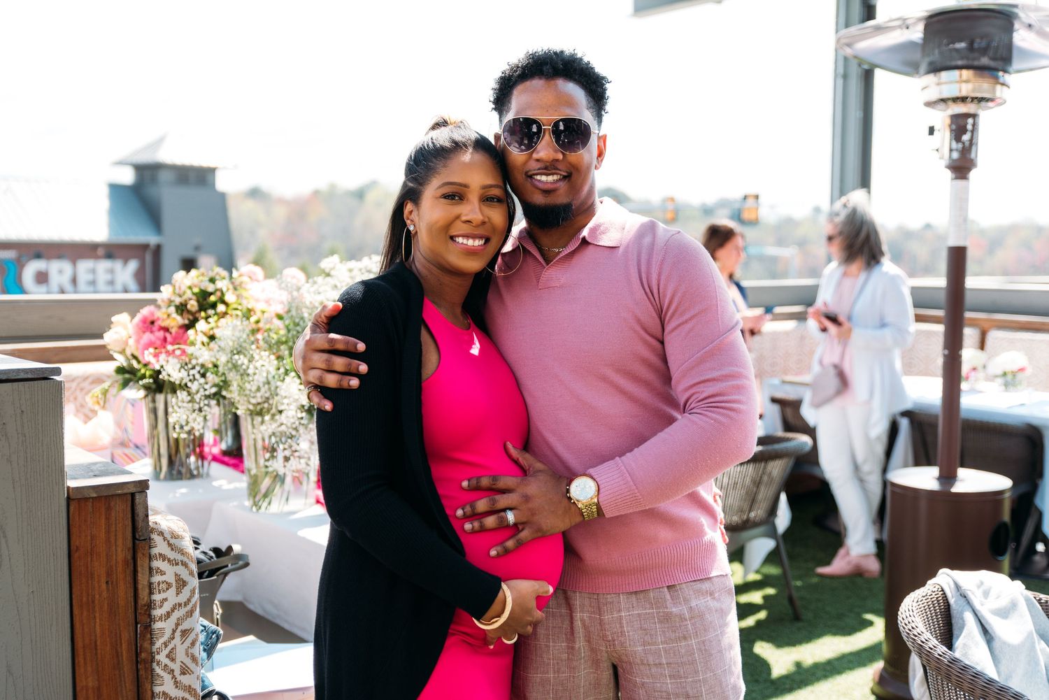 Guests enjoy a sunny outdoor celebration with drinks and flowers.