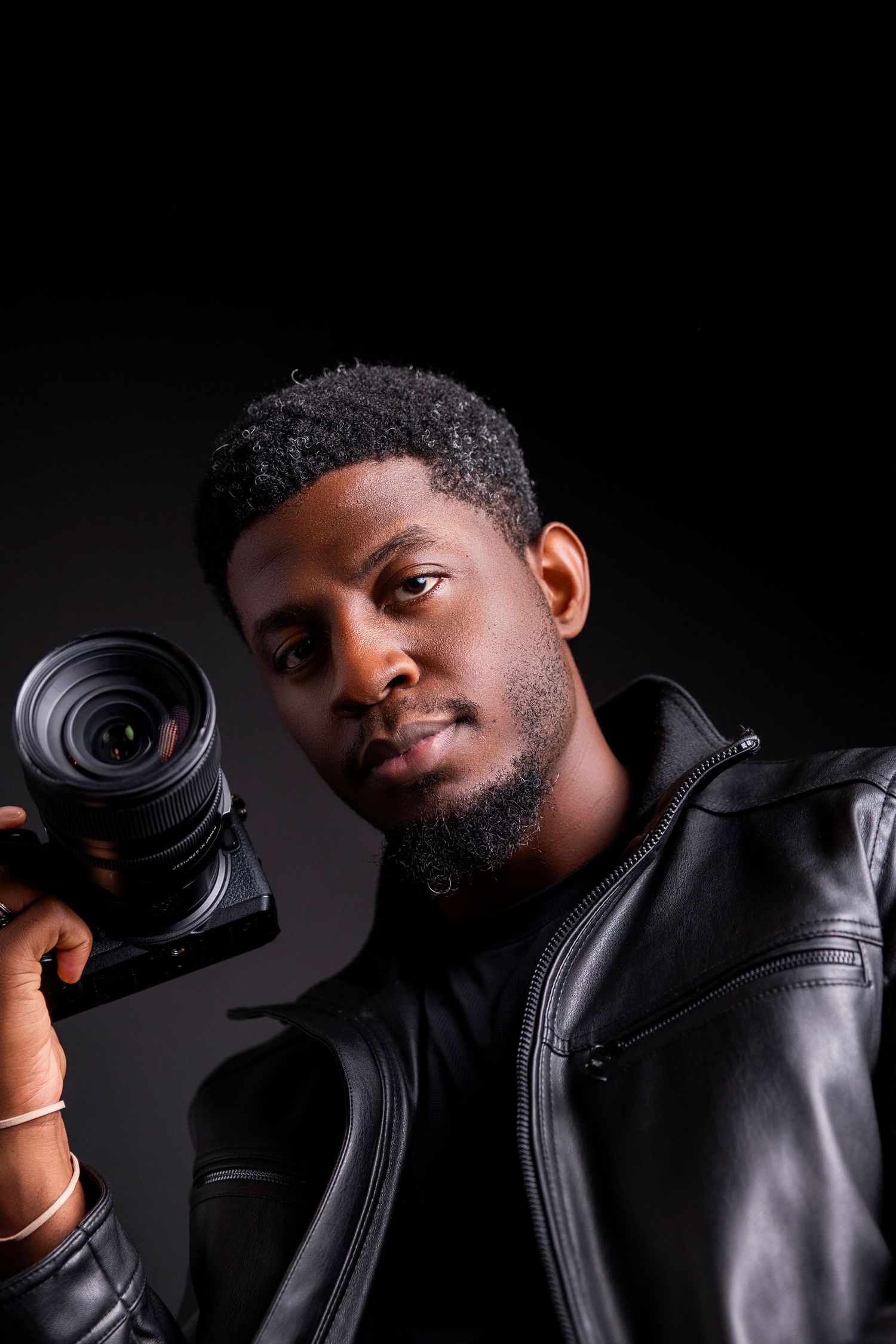 Portrait of photographer holding camera against dark background wearing leather jacket.