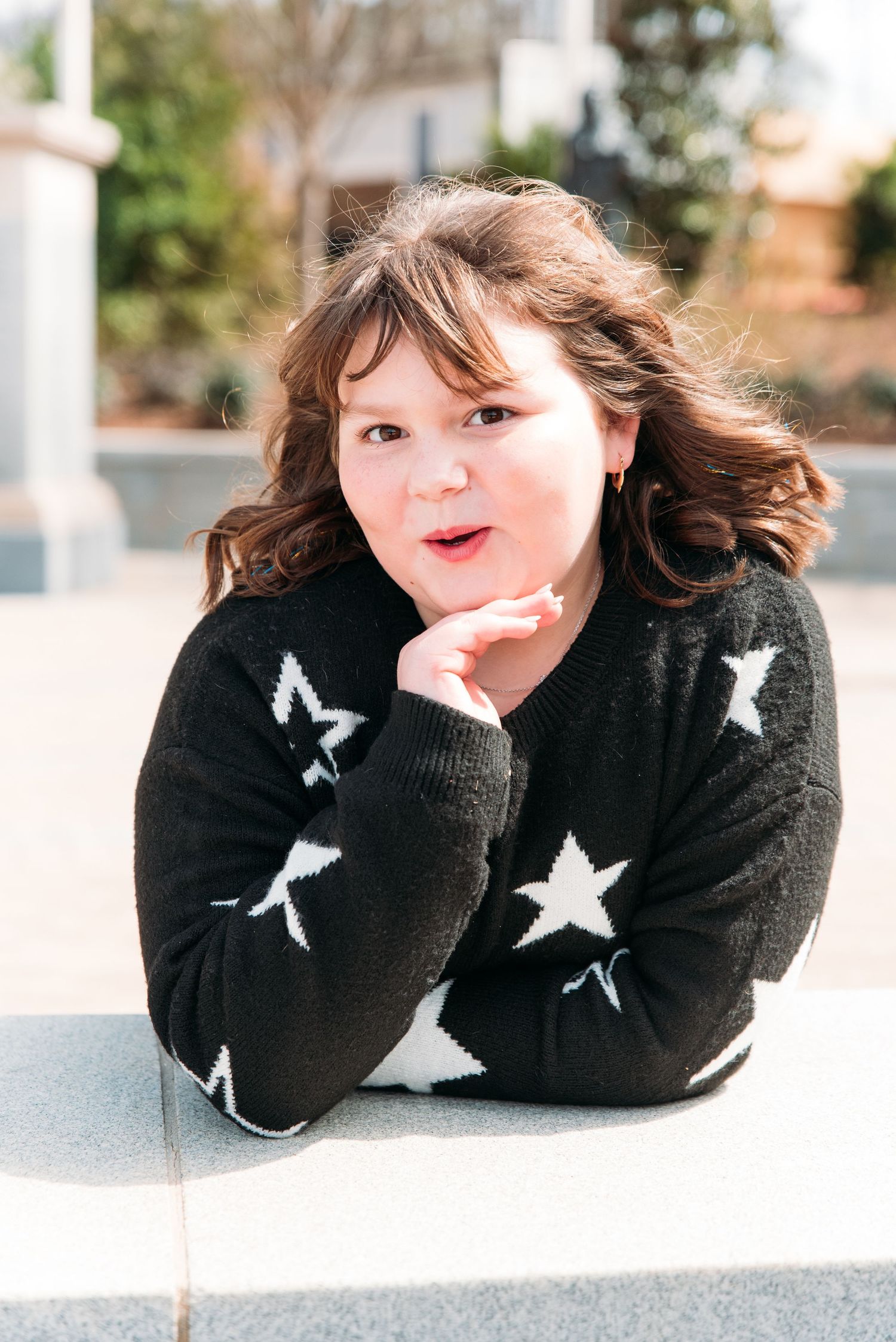 Portrait of person in black star sweater resting head on hand outdoors.