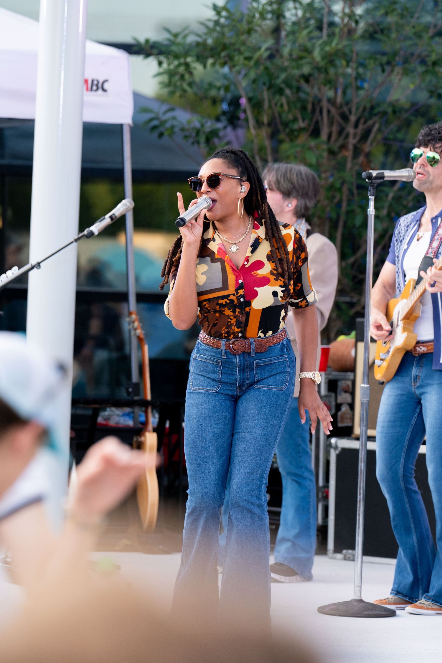 Band members in denim perform outdoors under white columned structure.