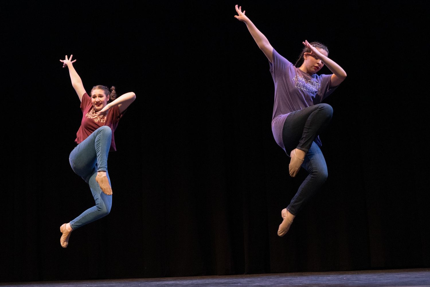 Contemporary dancers executing dynamic jumps and leaps against a black background.