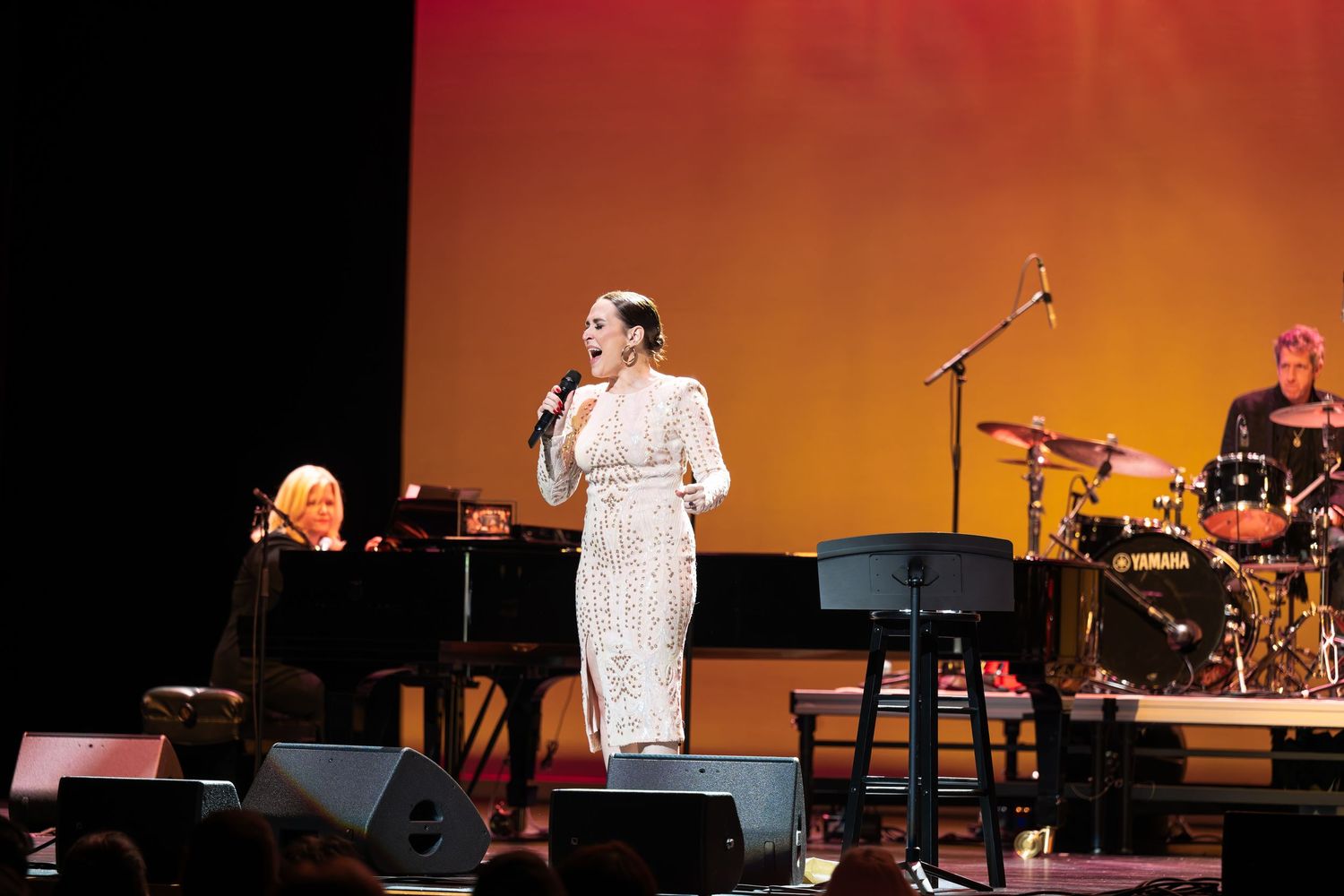 Concert performance on stage with warm orange lighting and musical instruments.