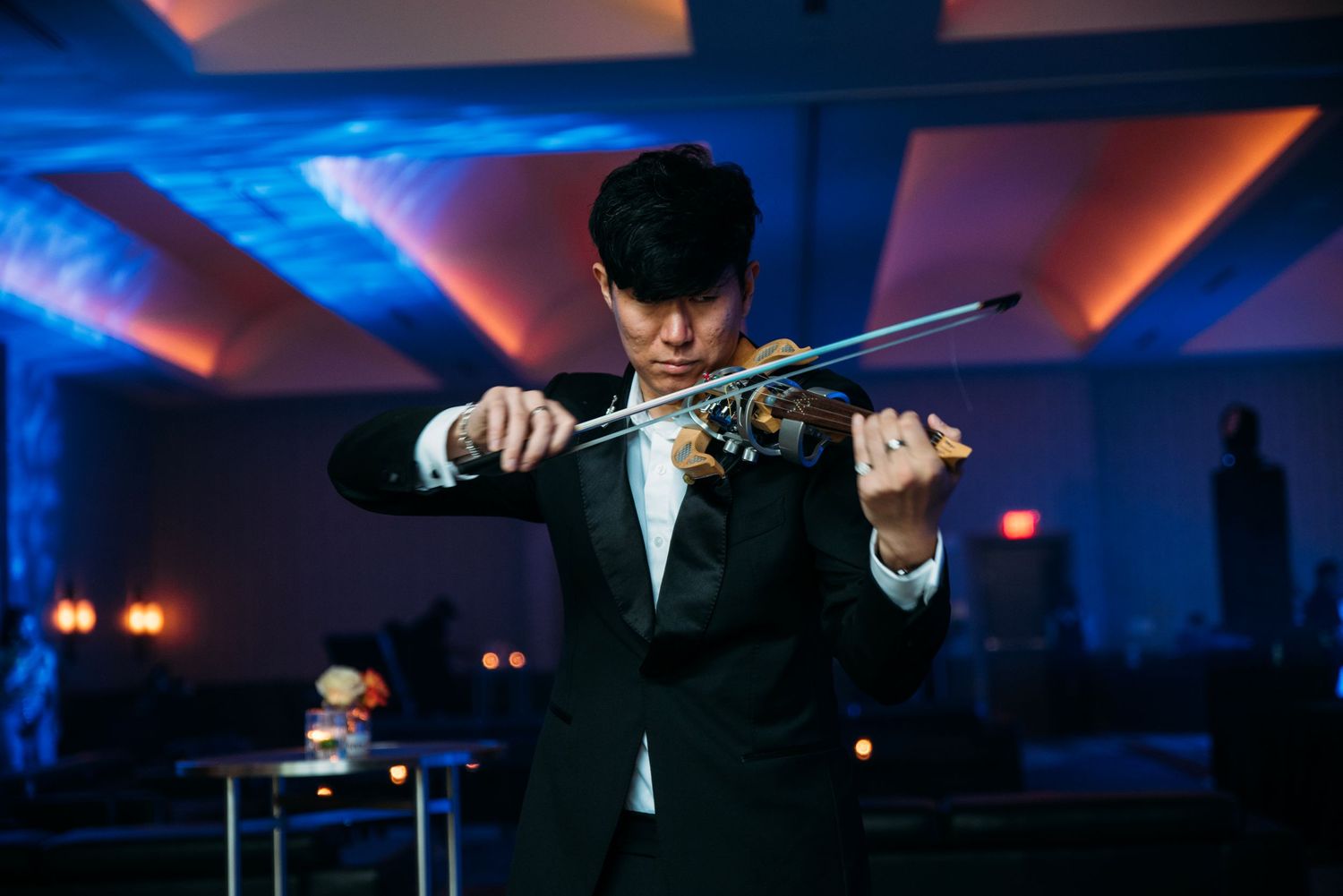 A violinist performs in formal attire under dramatic blue and red stage lighting.