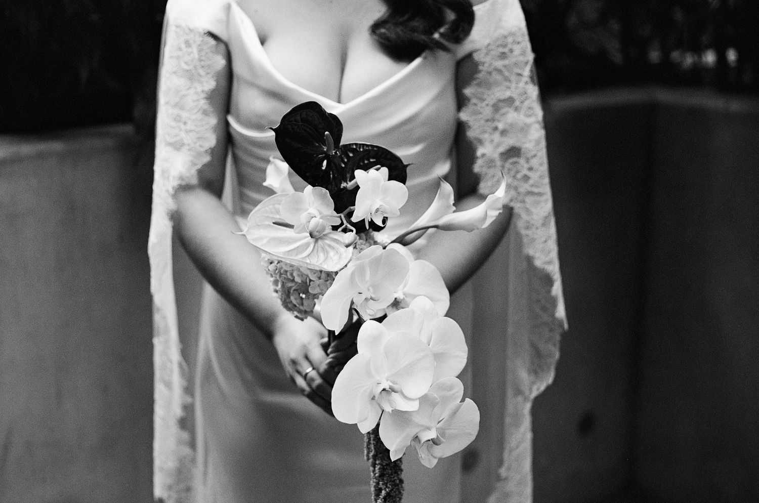 A bride in white dress holds a classic white orchid bouquet against a dark background.