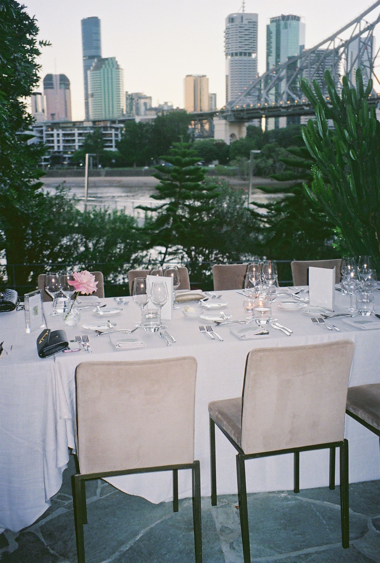 Elegant outdoor dining setup with city skyline and bridge view at dusk.
