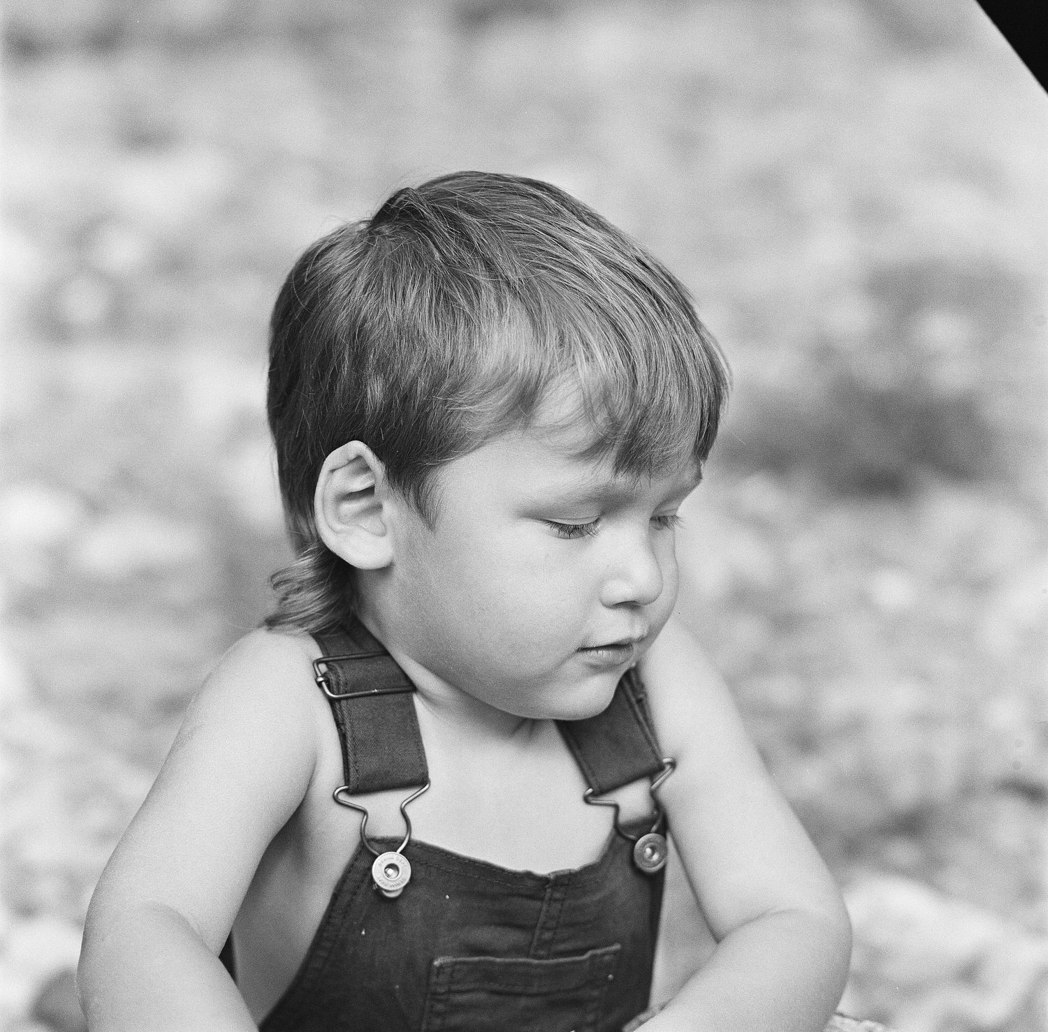 Black and white close-up of a small child wearing dark overalls with a contemplative expression.