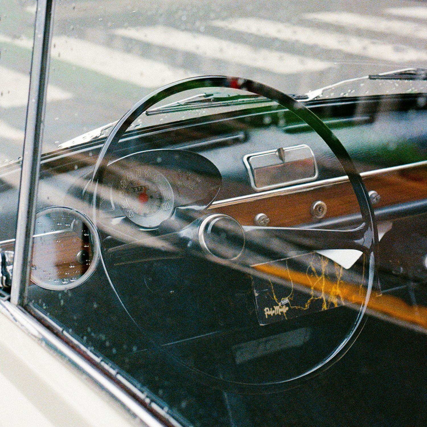 Classic car dashboard with vintage steering wheel and gauges through windshield.