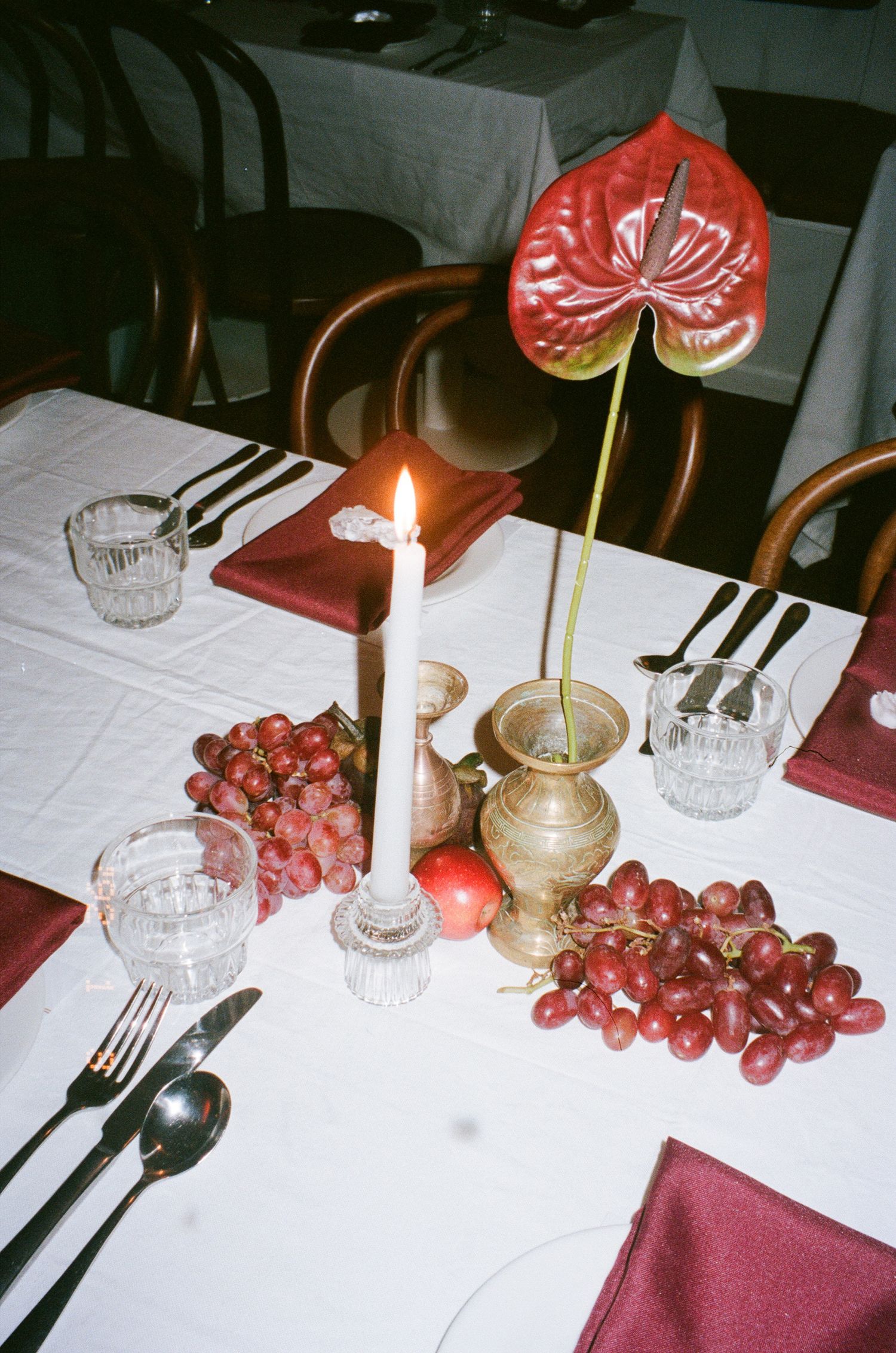 Elegant table setting with red grapes, white linen, lit candle, and red anthurium flower in vintage style photography.