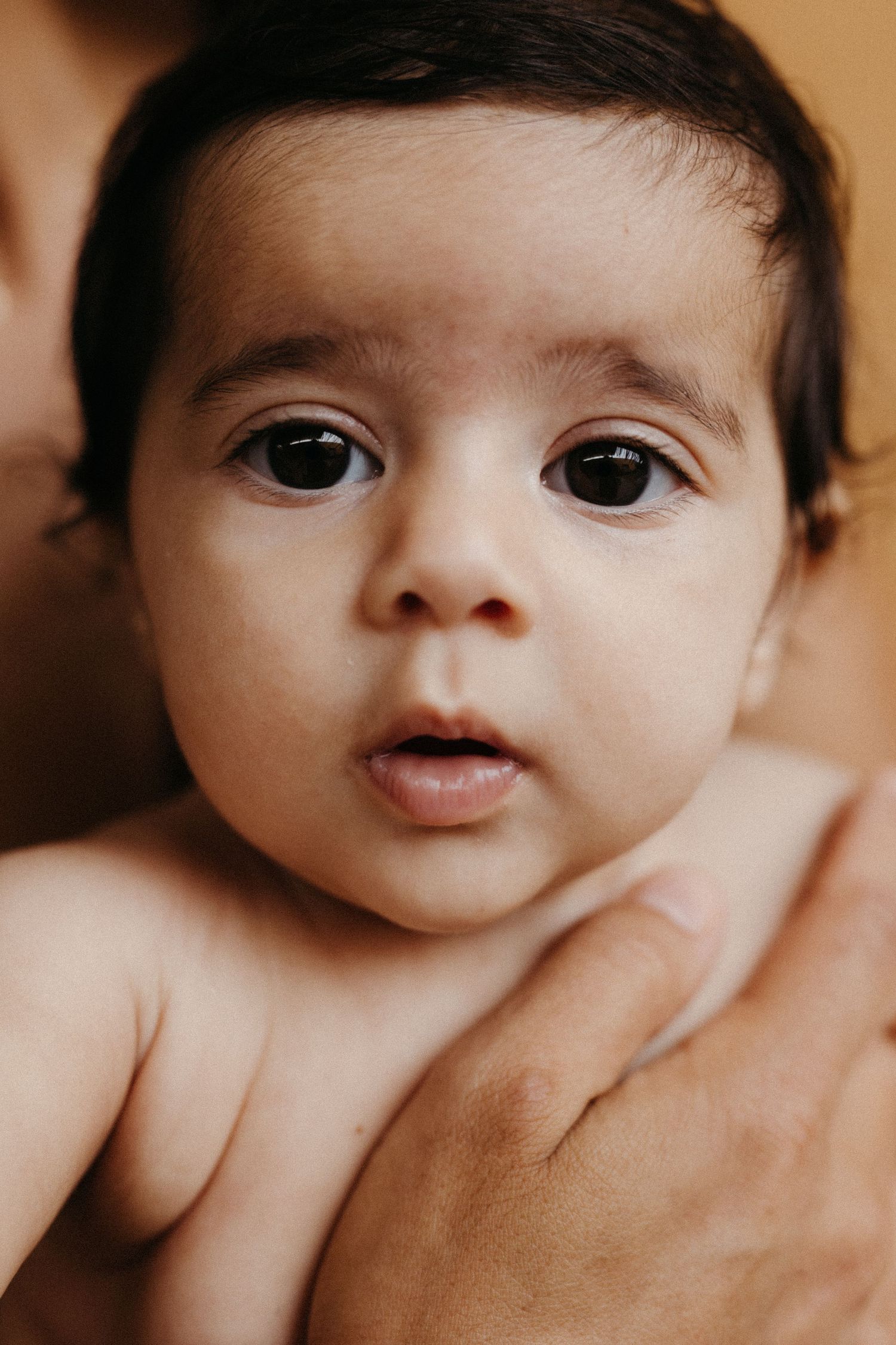Close-up portrait of a baby with wide dark eyes looking at the camera.