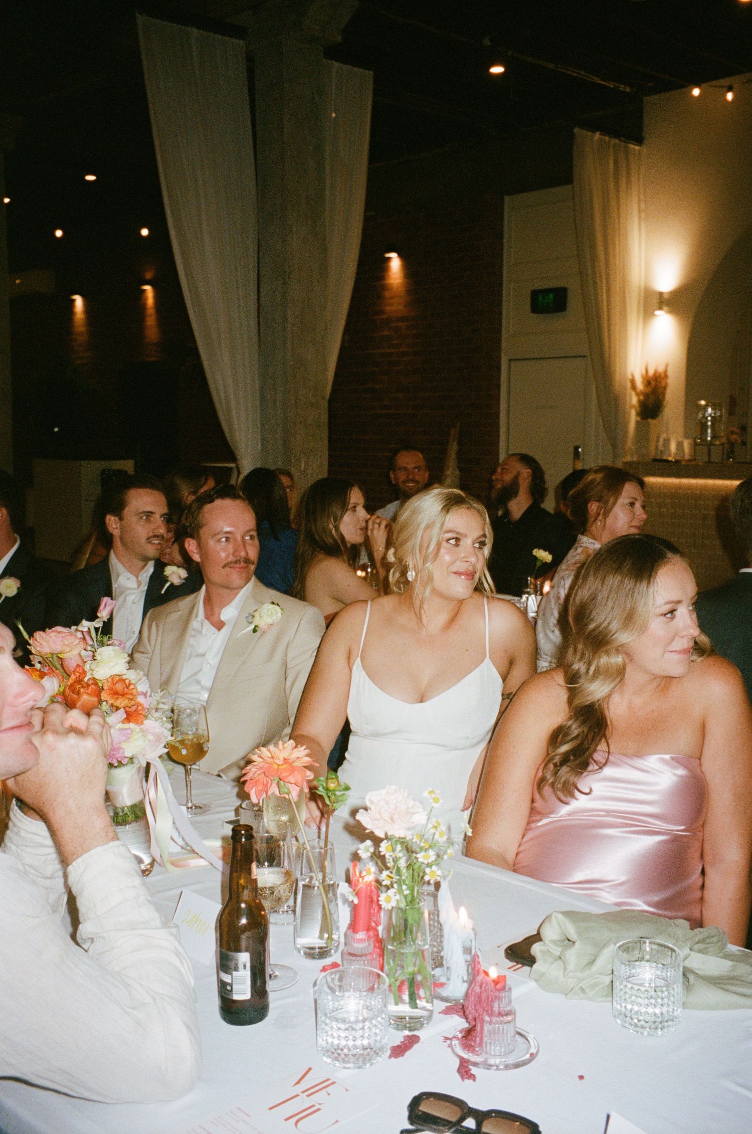 Guests seated at an elegantly decorated reception table with pink floral centerpieces.