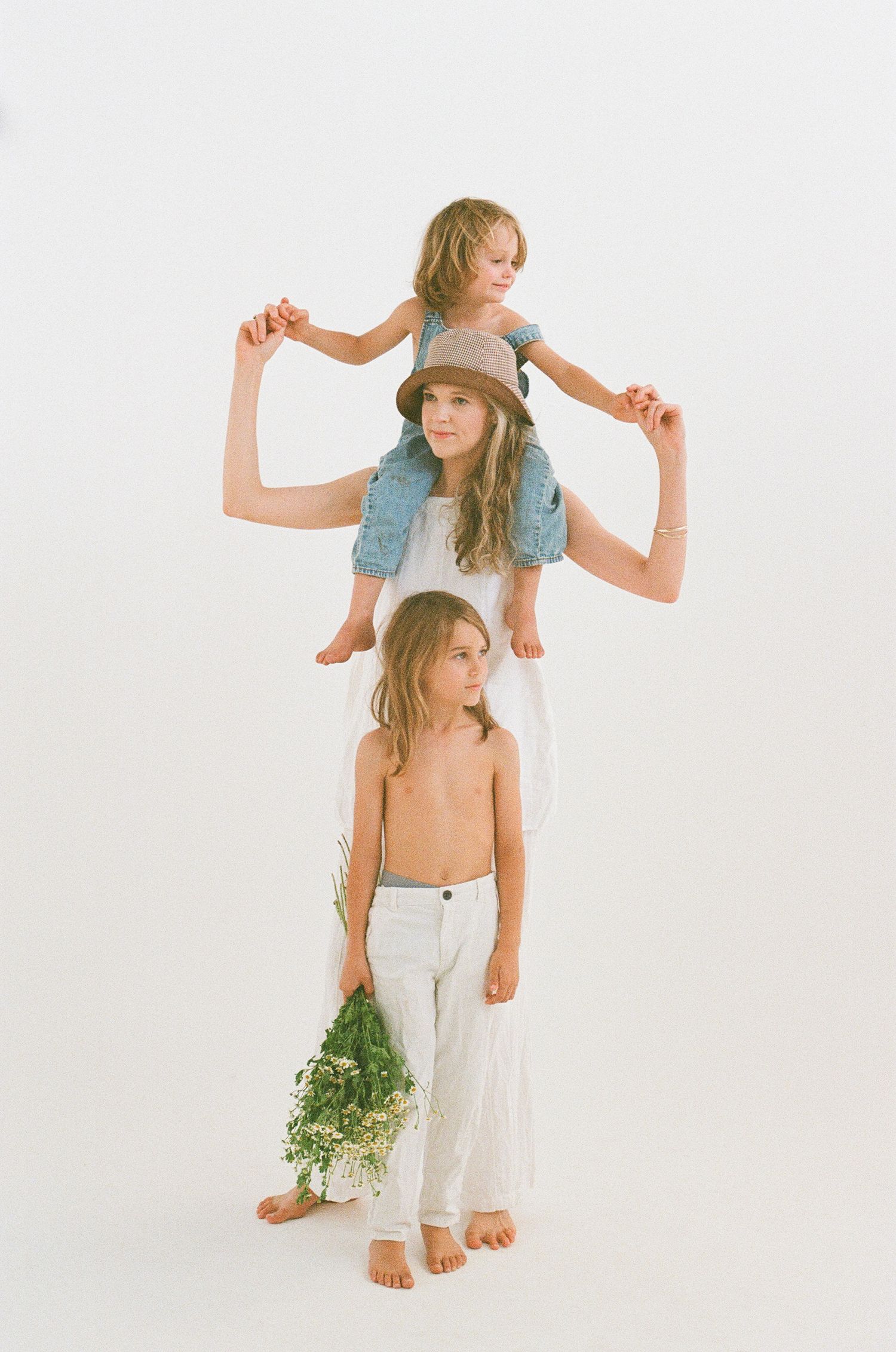 Studio portrait of three people in white clothing posed in a vertical stack.
