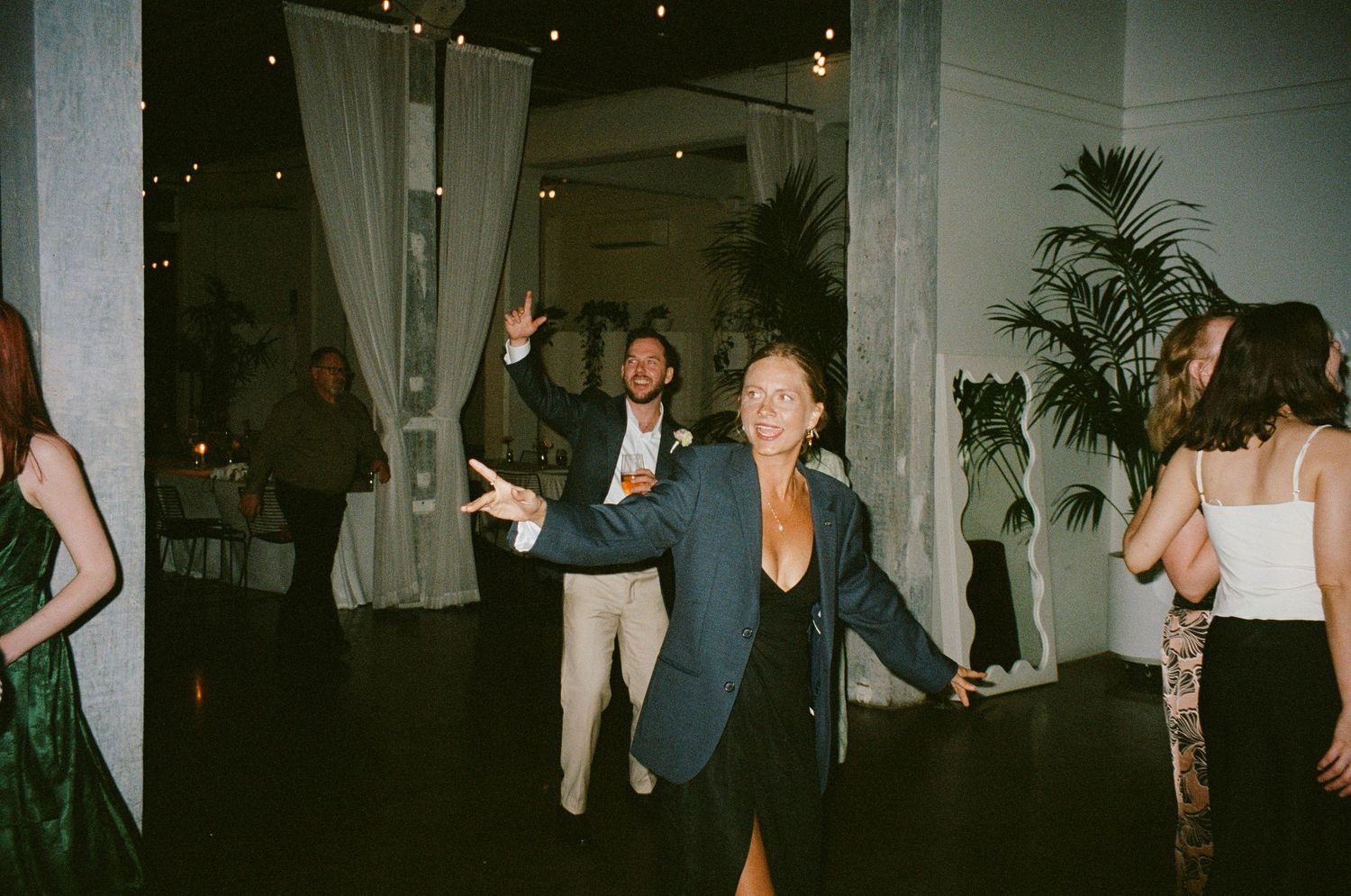 Party guests dance and celebrate on a dimly lit dance floor with white drapes in the background.