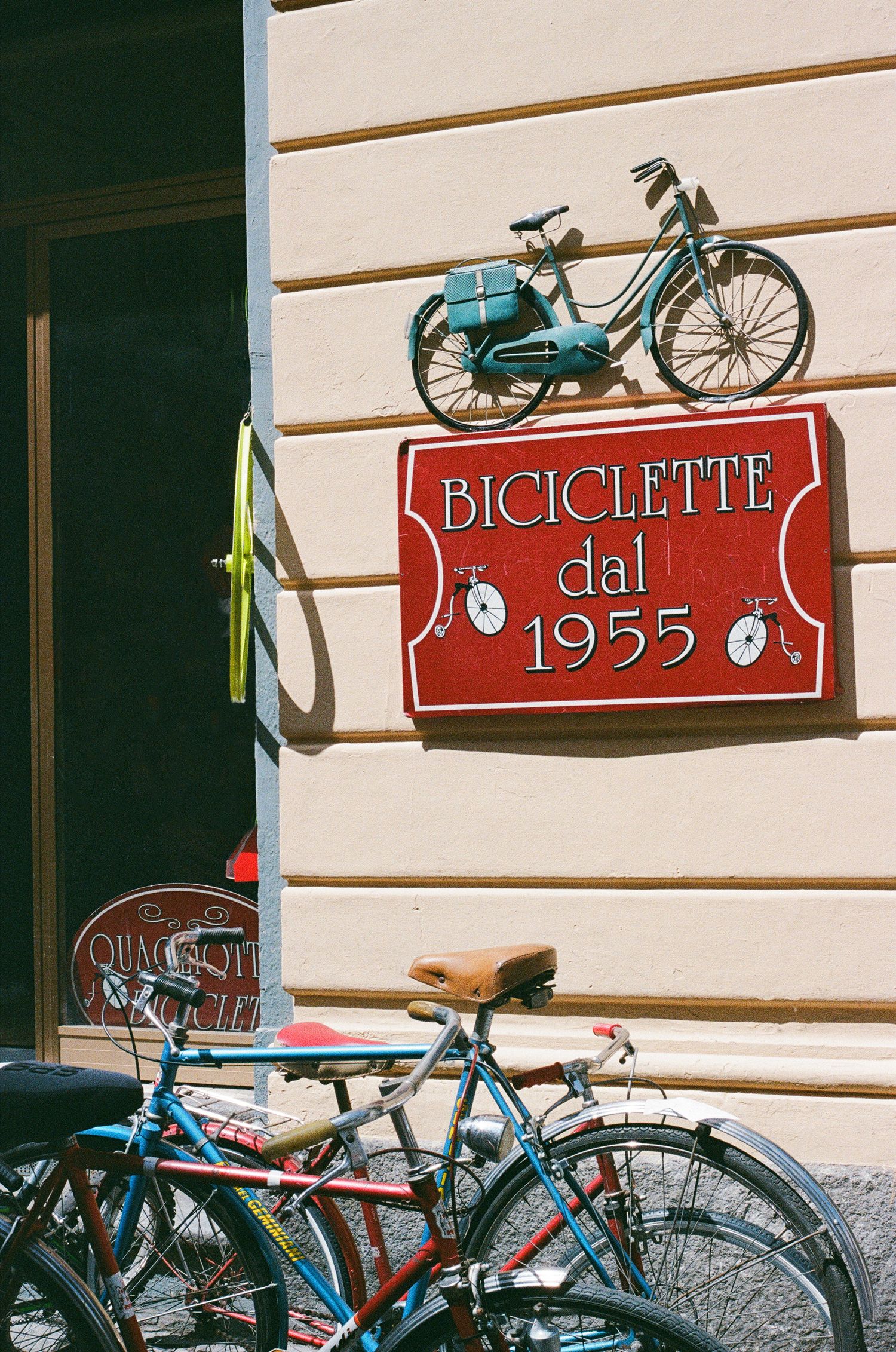 Vintage bicycle shop sign with blue bikes parked outside against a cream-colored building.