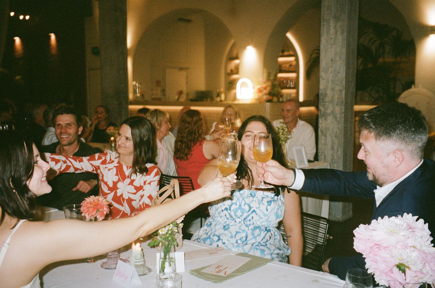 Wedding guests toasting and celebrating at a dimly lit reception venue.