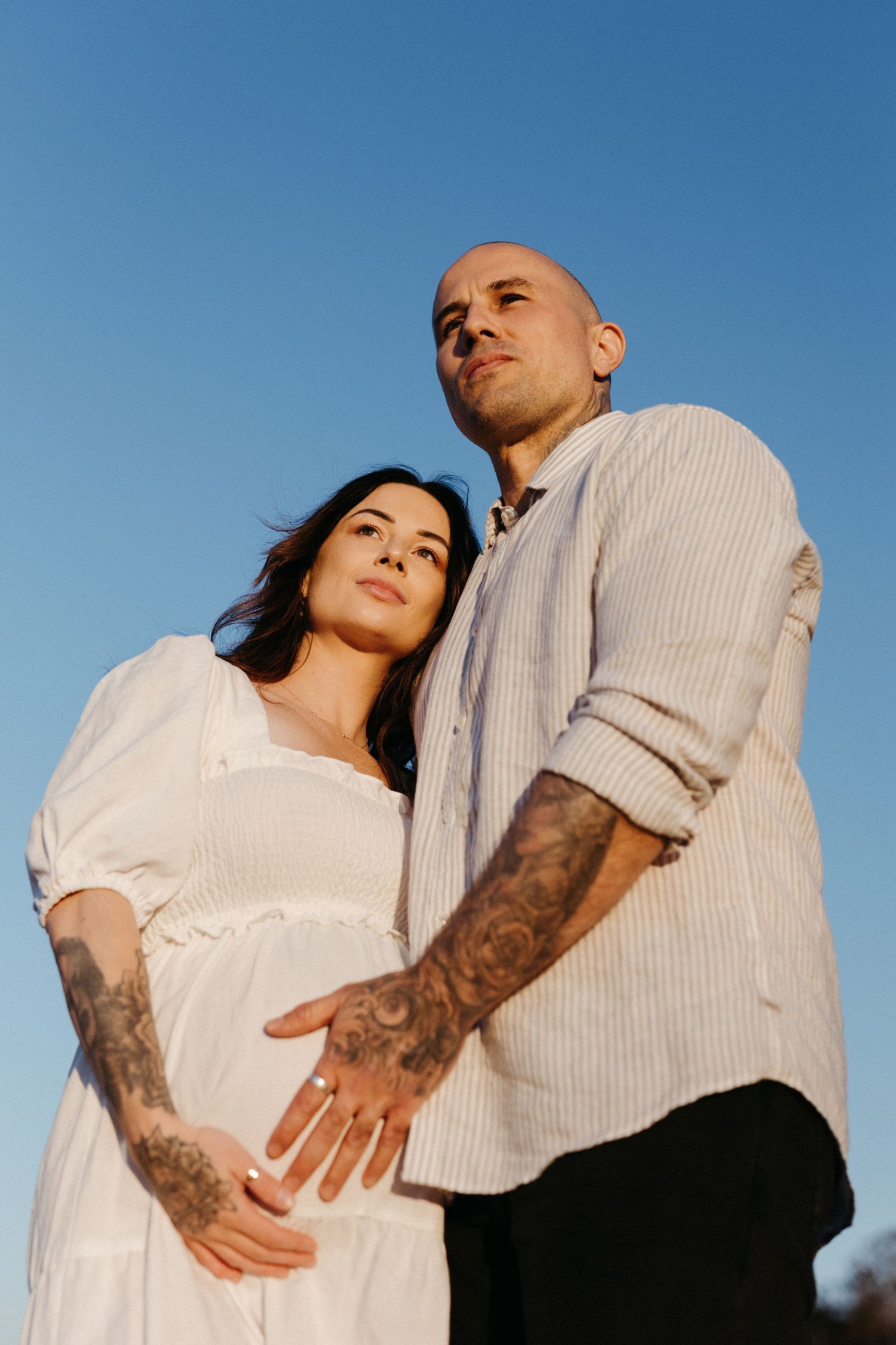 A romantic couple in white and black outfits embrace against a blue sky in a series of intimate poses.
