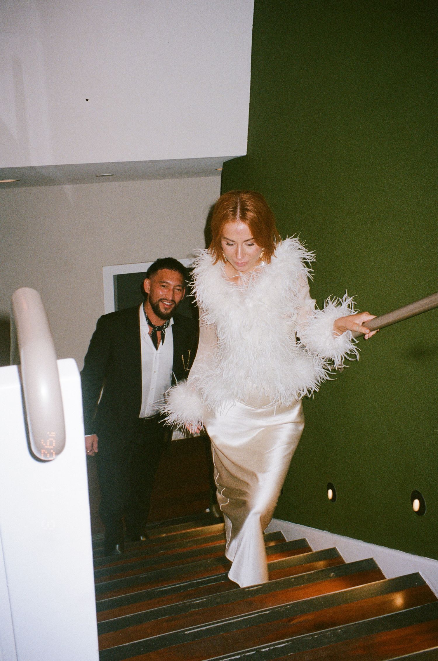 Elegantly dressed couple descending a staircase at a formal event.