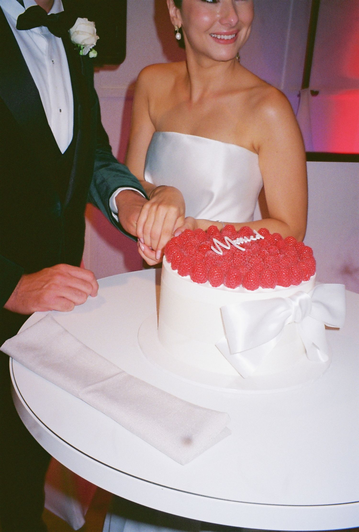 A wedding cake topped with fresh red raspberries being cut during the reception.