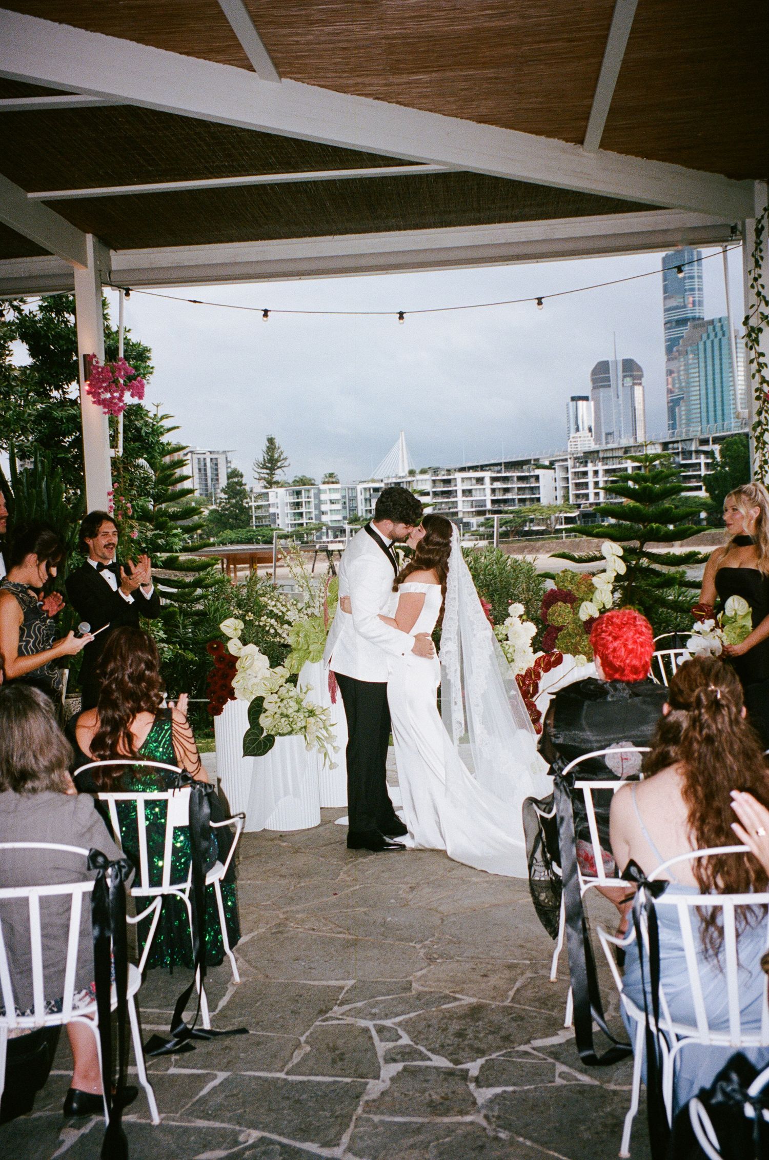 Wedding reception celebration under a covered outdoor venue with guests seated at tables.