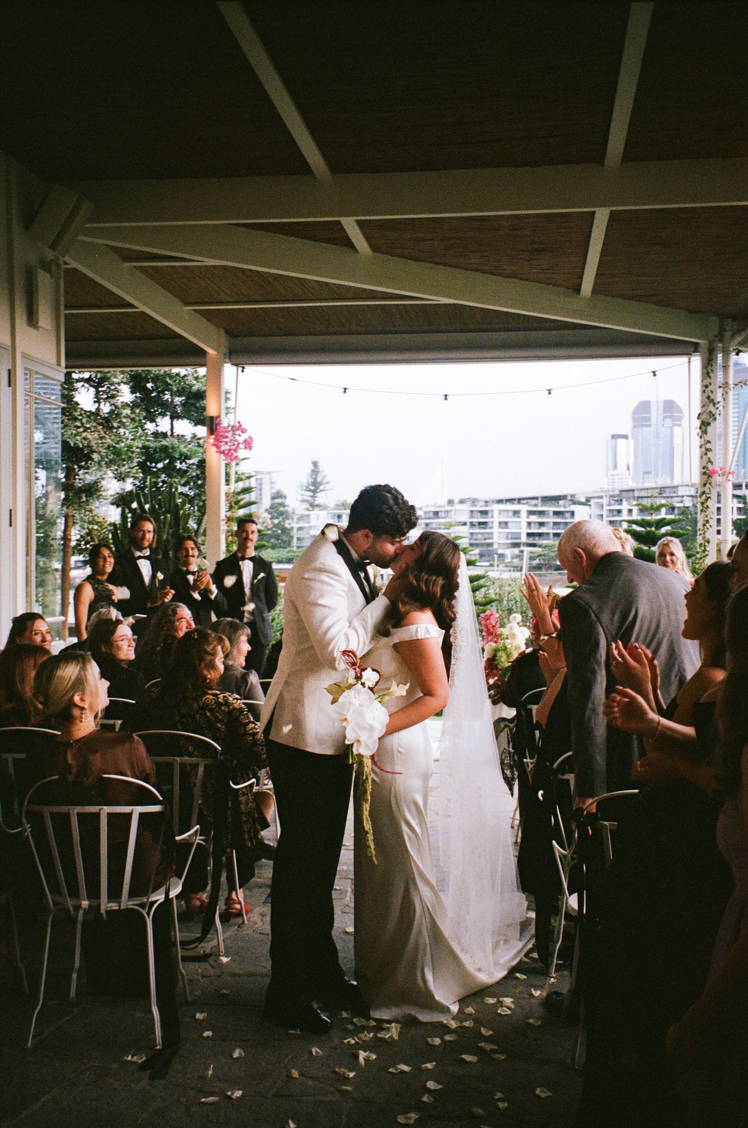 A crowded wedding reception venue with guests dancing and celebrating under a covered outdoor space.