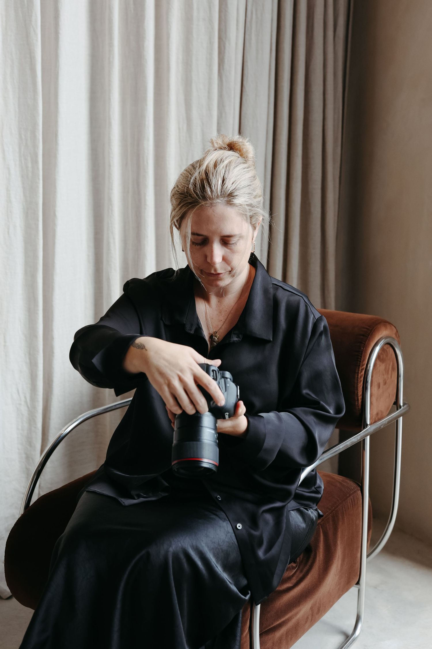 Professional photographer in black attire reviewing camera while seated in leather chair.