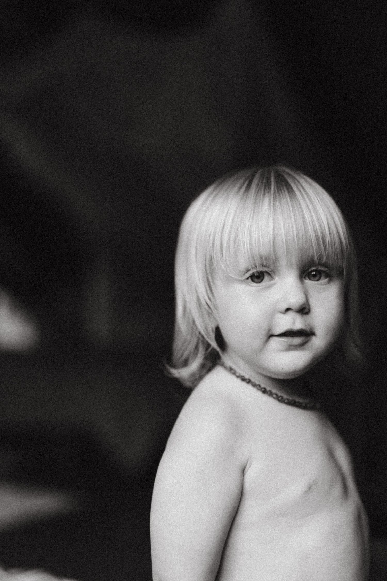 Black and white portrait of young child wearing necklace.